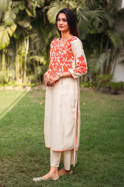 Side view of an Indian model in a beige chanderi kurta with orange floral patchwork, complemented by beige palazzo.