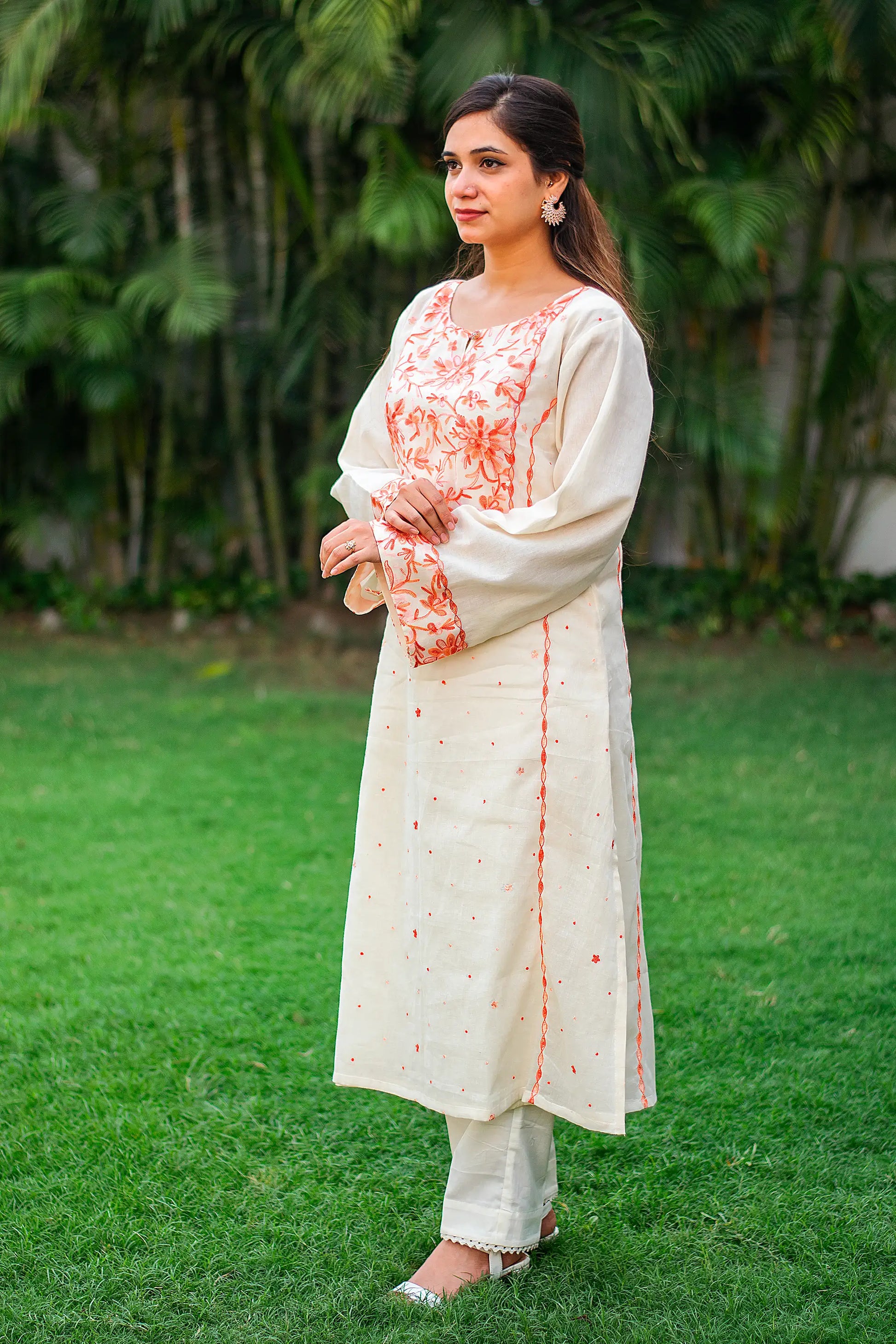 Side view of an Indian model in an off-white kurta with peach floral embroidery, paired with matching trousers. 