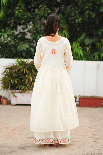 Back pose of a young Indian woman in an off-white cotton Bahaar-e-Chinaar frock kurta set with matching palazzo pants and dupatta.