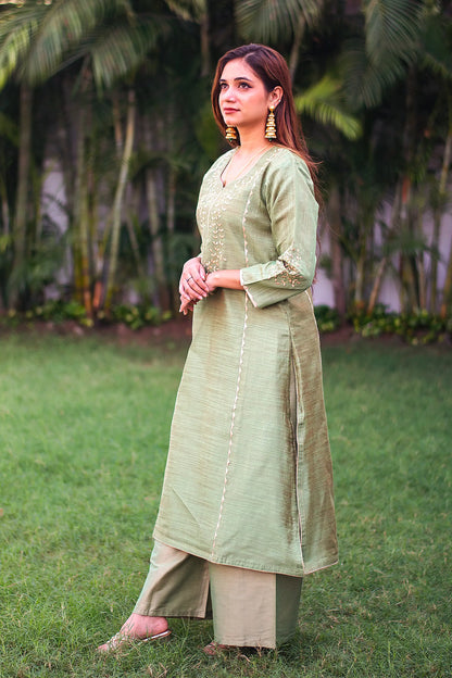 Indian model gives a side pose in a green jute silk kalidar kurta with beige applique work and a green palazzo.