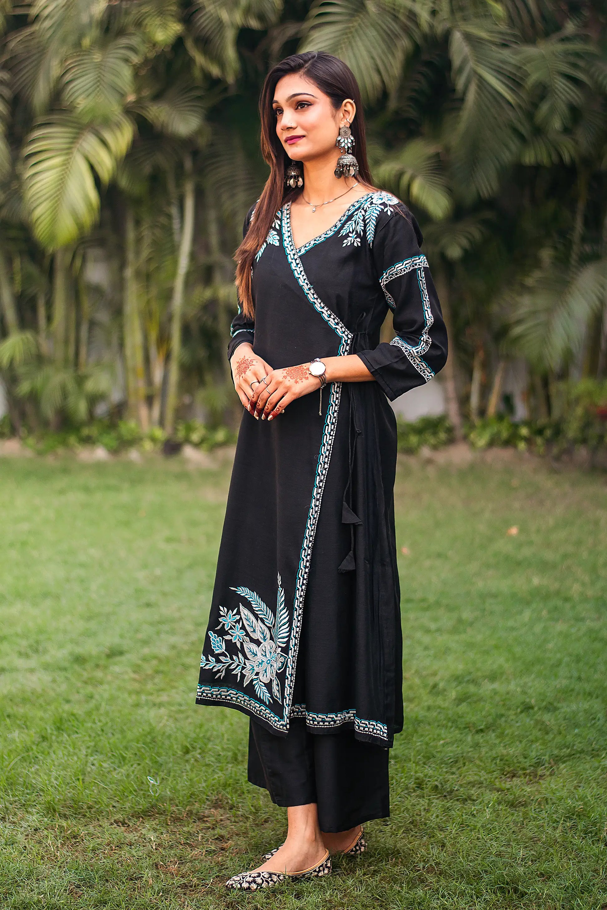 Side view of an Indian model in a black chanderi angrakha kurta with white and blue embroidery, paired with black palazzo