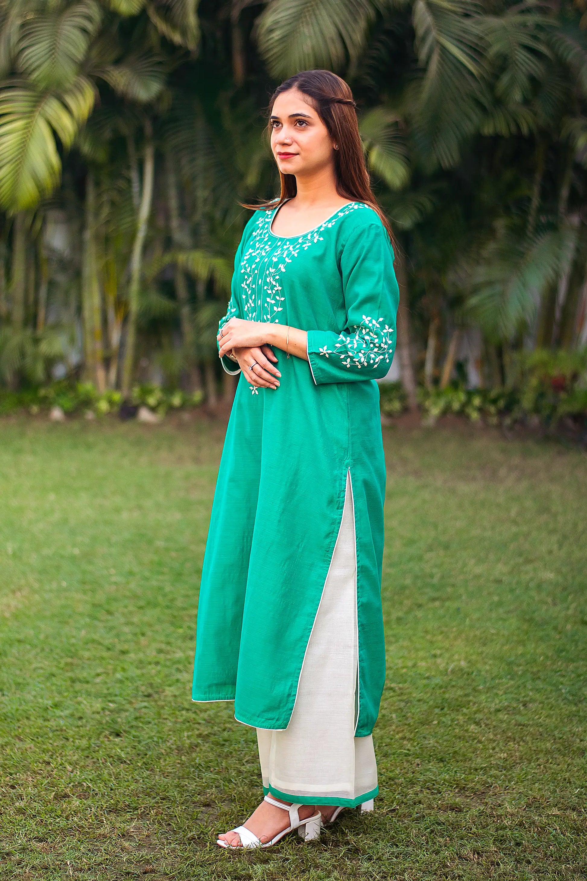 An Indian girl in a side pose wearing a green Chanderi kurta with applique work and white palazzo, full length is visible.