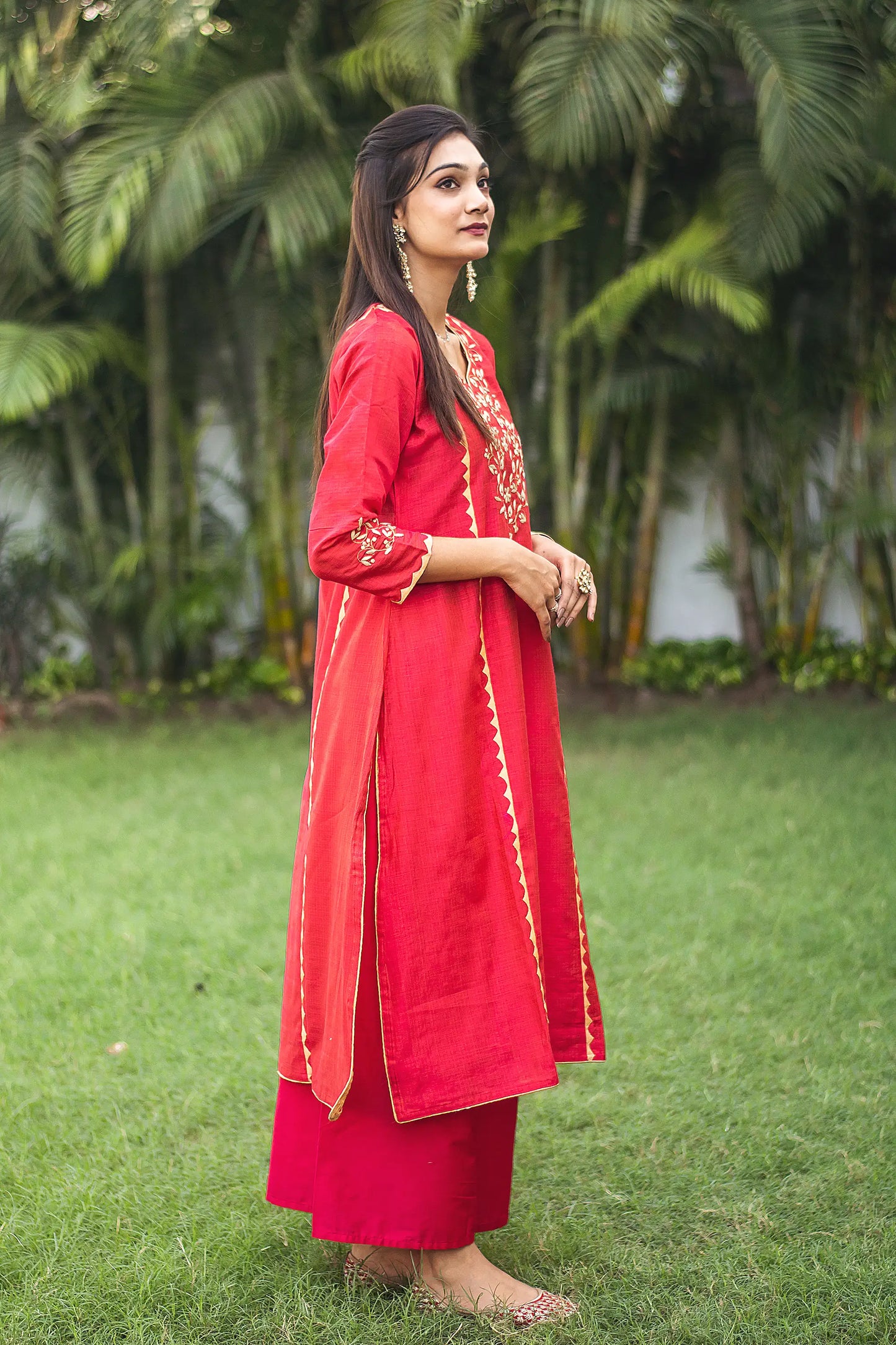 Indian lady poses sideways, wearing a red jute silk kalidar  kurta with beige applique work and a red palazzo