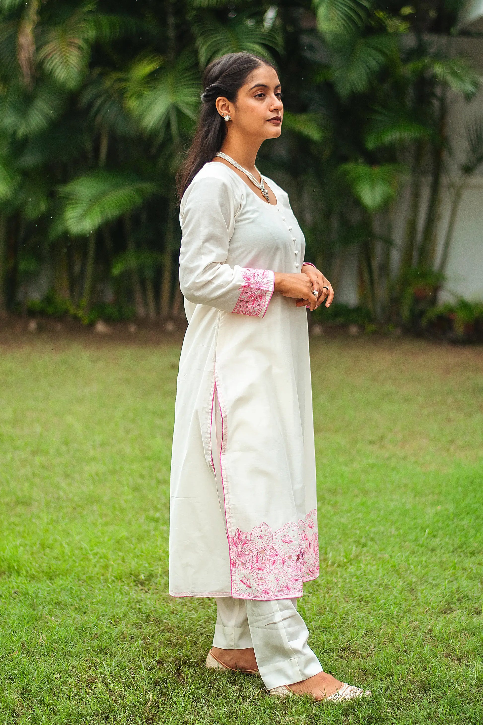 Side view of an Indian woman wearing an off-white chanderi kurta with pink floral cutwork and sequins, complemented by off-white trousers