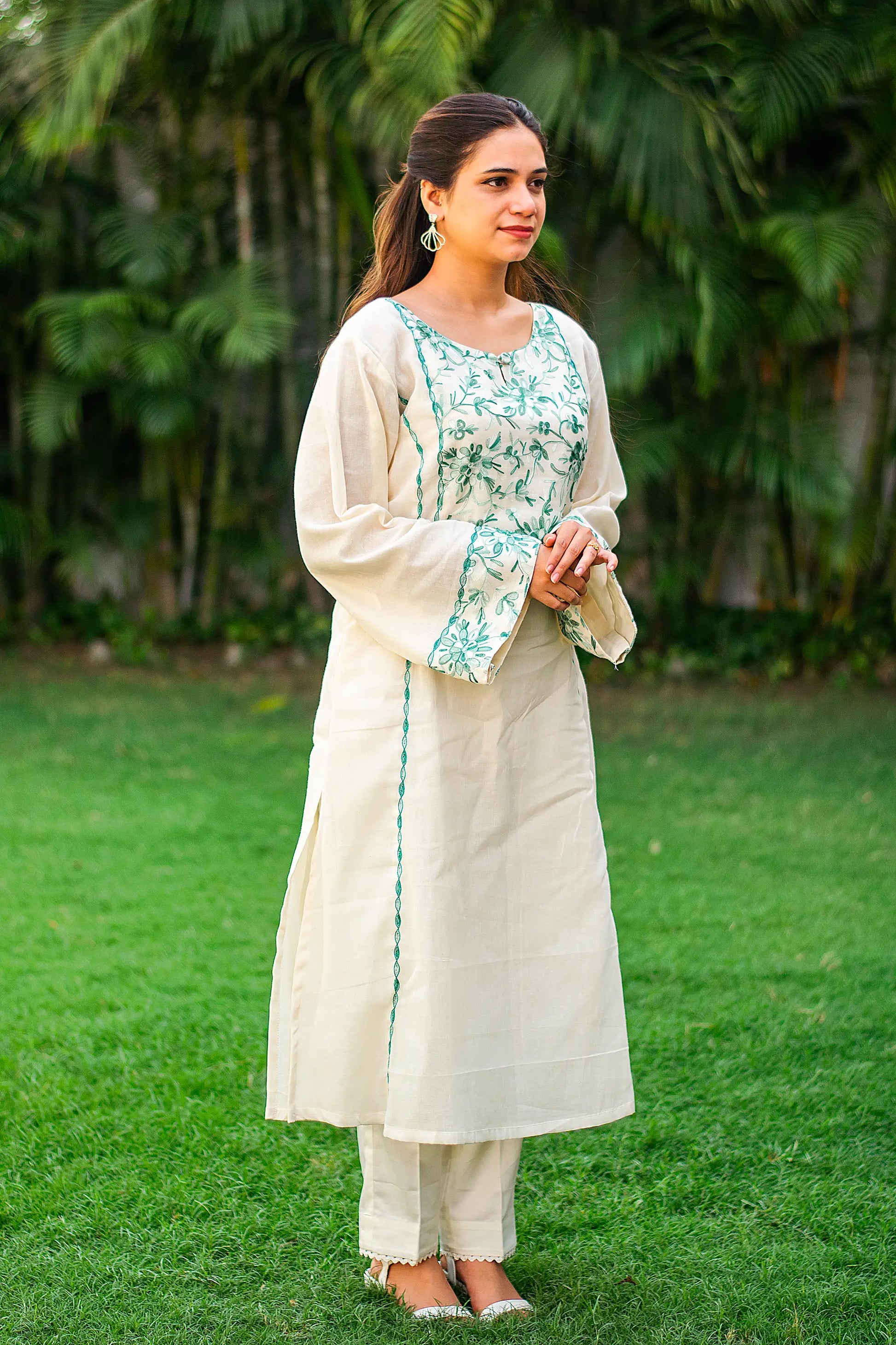 Side view of an Indian model in an off-white kurta with green embroidery and matching trousers. 