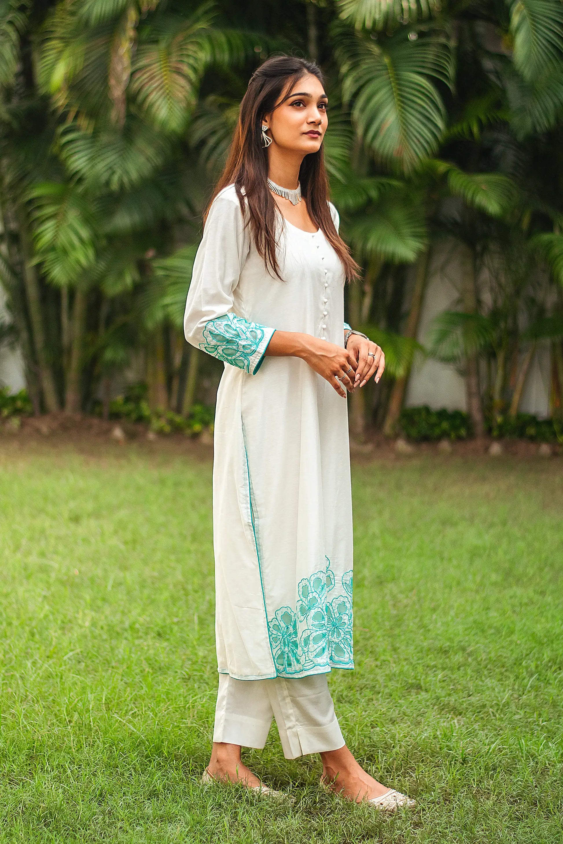 Right side view of a model wearing the off-white Chanderi suit with cyan green floral cutwork, highlighting the suit's elegant silhouette