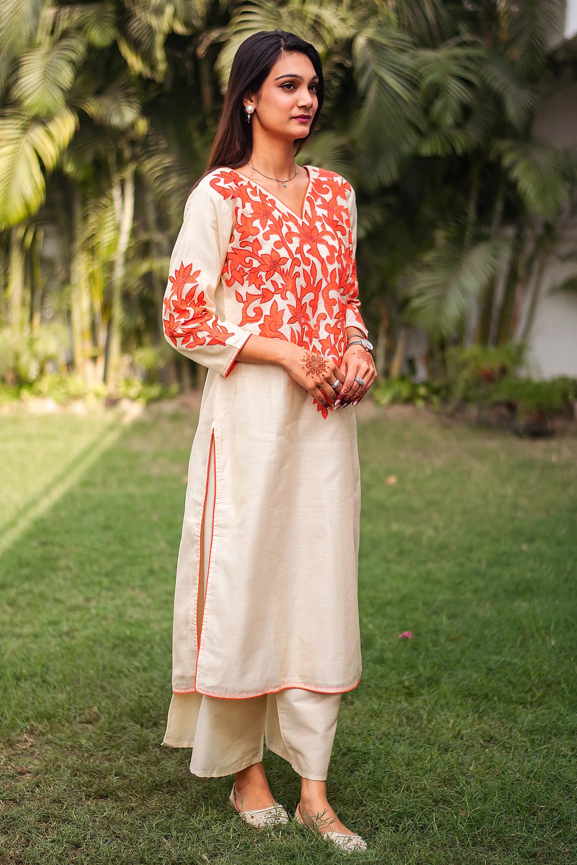 Side view of an Indian model as she poses dressed in beige kurta with orange patchwork and matching beige palazzo.