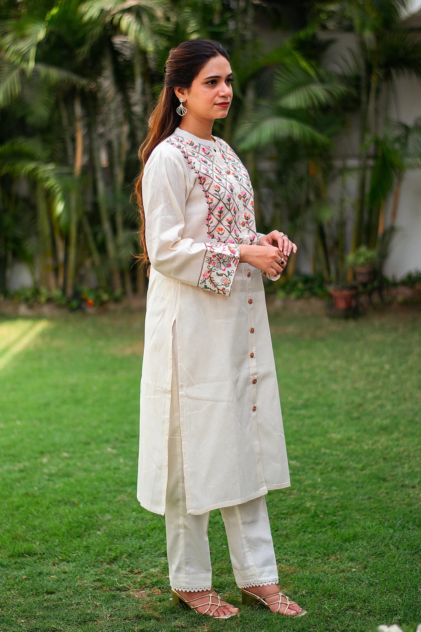 Side view of an Indian girl dressed in an off-white cotton kurti with floral Kashmiri embroidery, along with matching trousers.