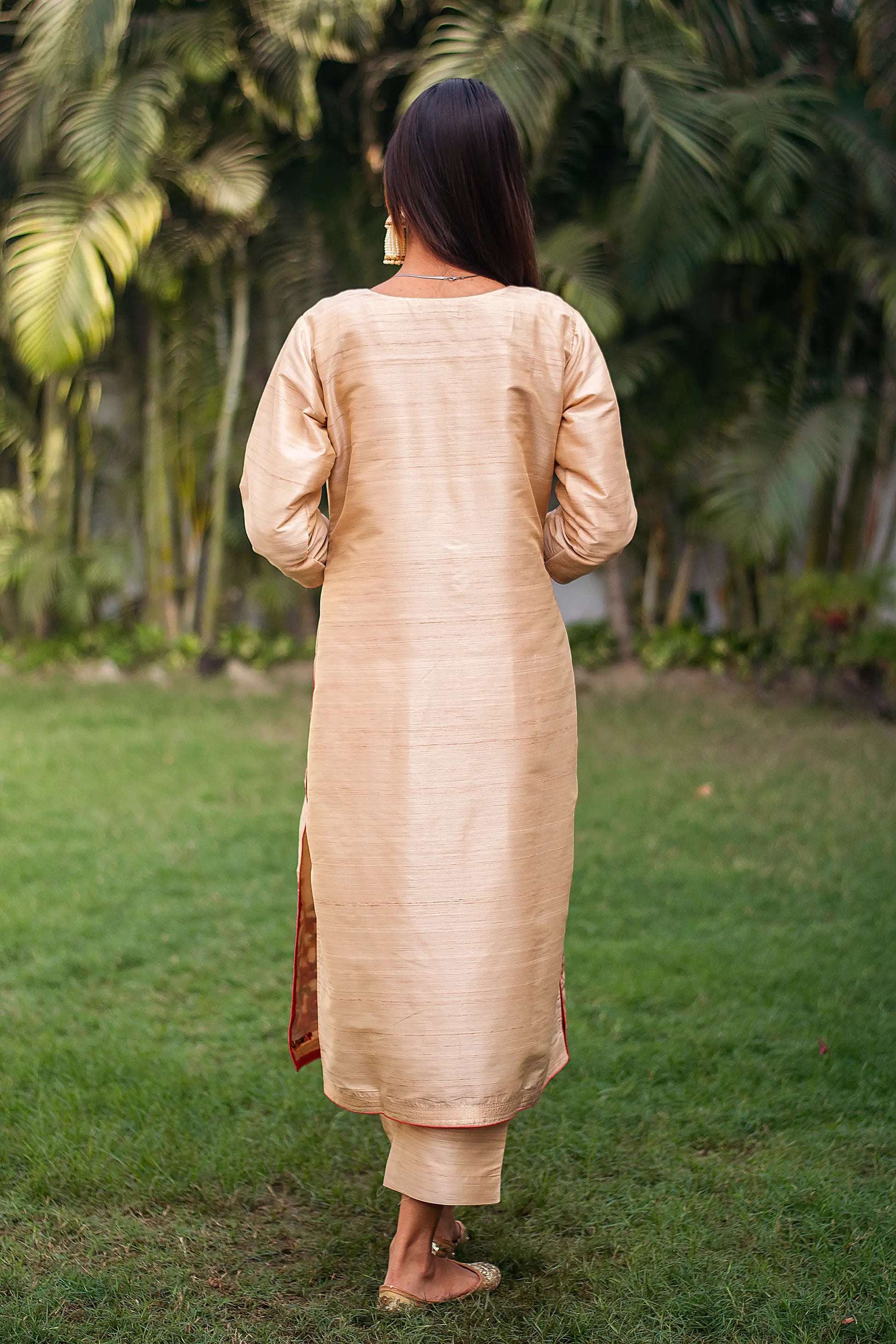 Back view of an Indian model wearing a beige silk kurta with resham work, paired with beige trousers.