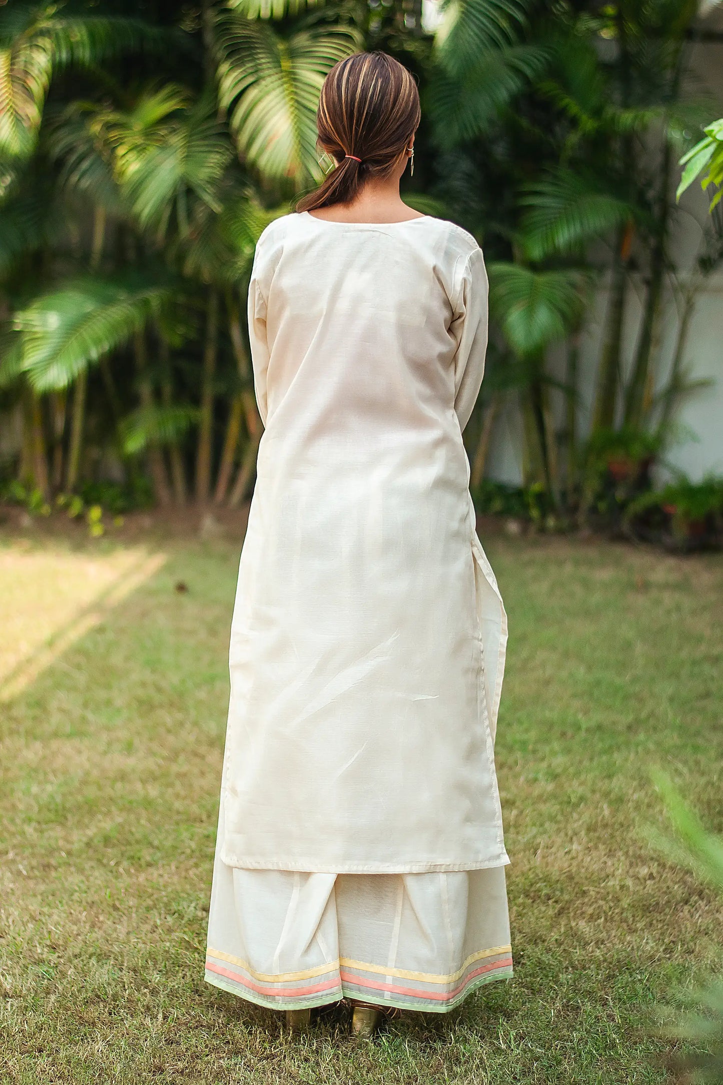 Back view of an Indian model in an off-white chanderi kurta with pastel piping and matching palazzo.