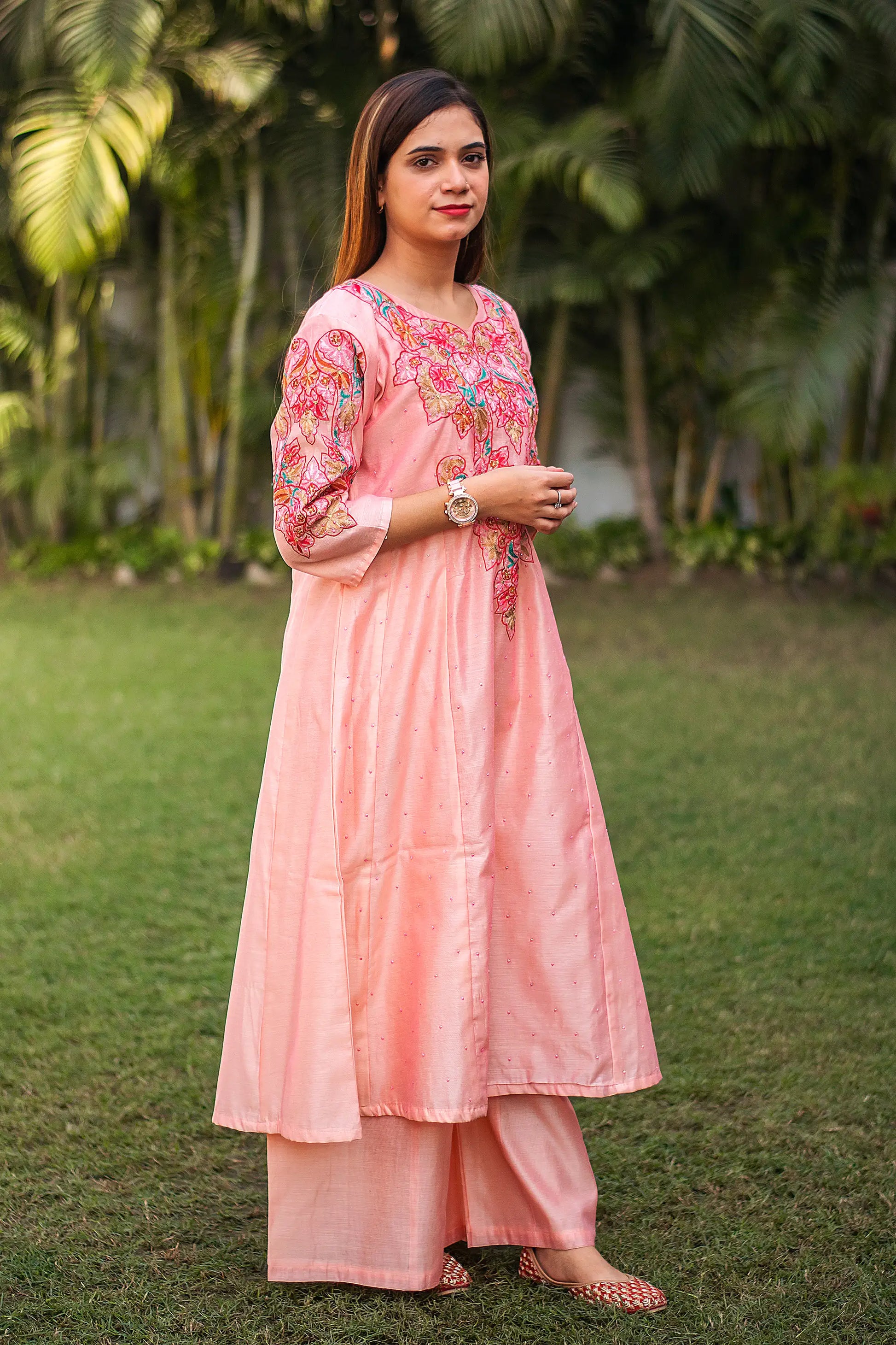 Indian model in a side pose, wearing  a peach A-line kurta with multicoloured resham work and matching palazzo.