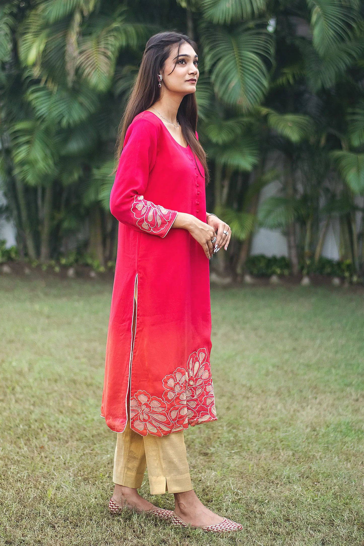 Side pose of an Indian model wearing a red organza kurta with gold floral cutwork, paired with gold brocade trousers.