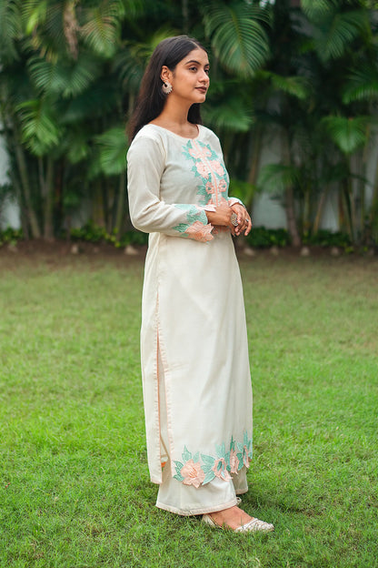 Side profile of an Indian model in a cream chanderi kurta showcasing peach floral patchwork, along with cream palazzo.