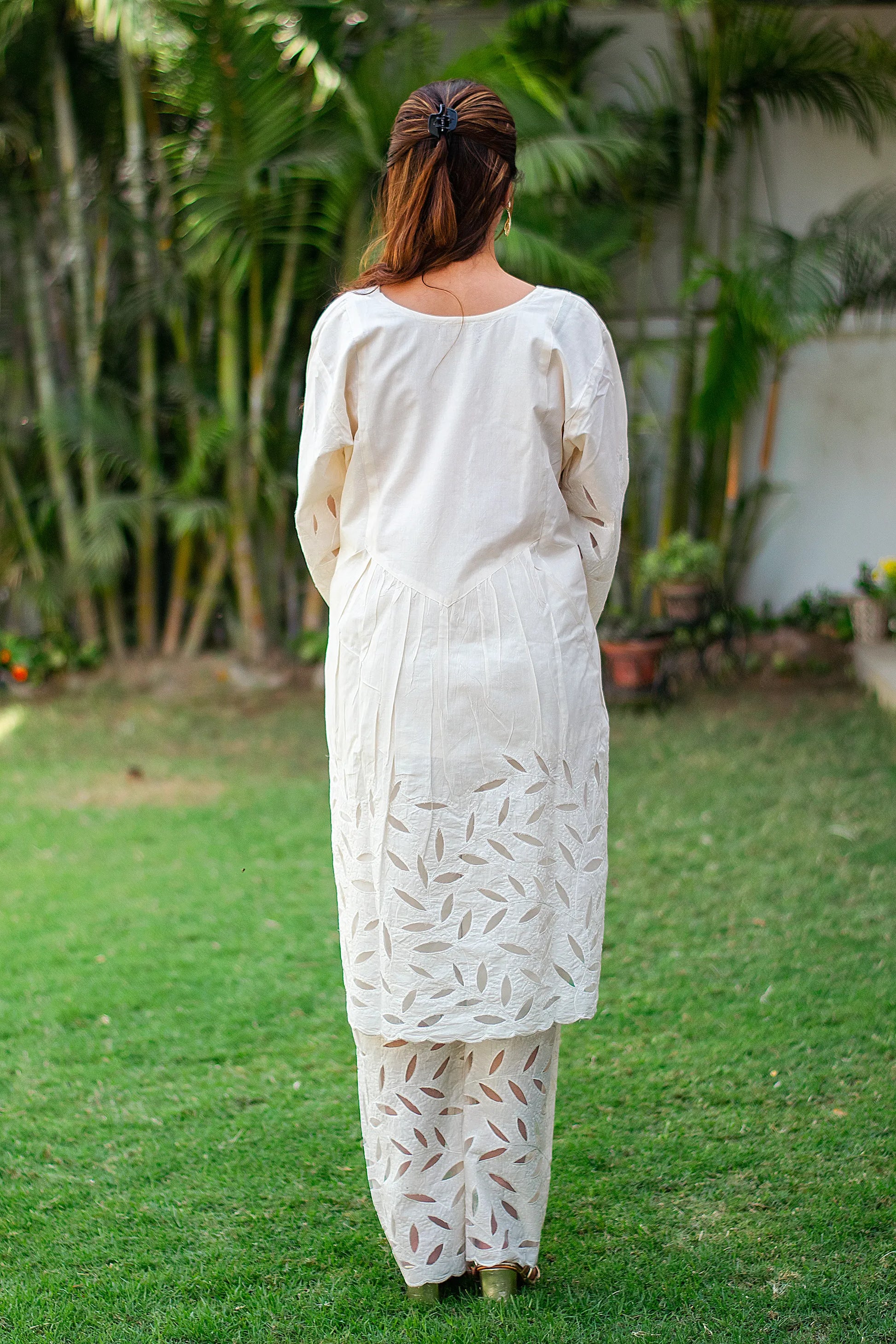 Back view of an Indian model wearing an off-white kurta set with embroidered detailing on the hem and cuffs.