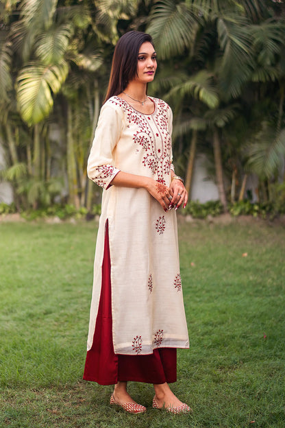 Indian model in a side pose,dressed in a beige kurta with maroon paisley motifs and contrasting maroon palazzo.