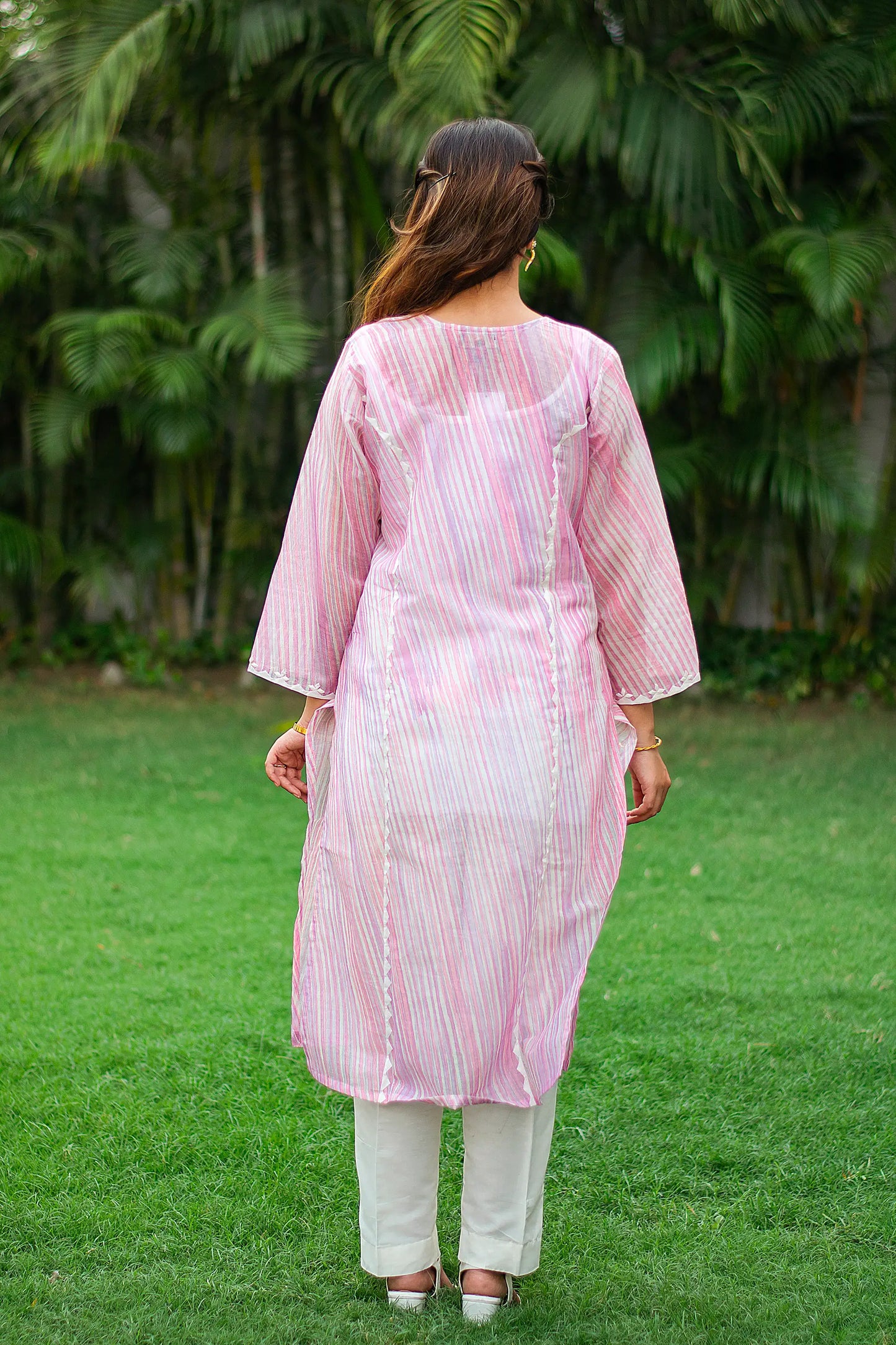 Back view of an Indian model wearing a light pink kurta with applique work along the kali joints, paired with white trousers.