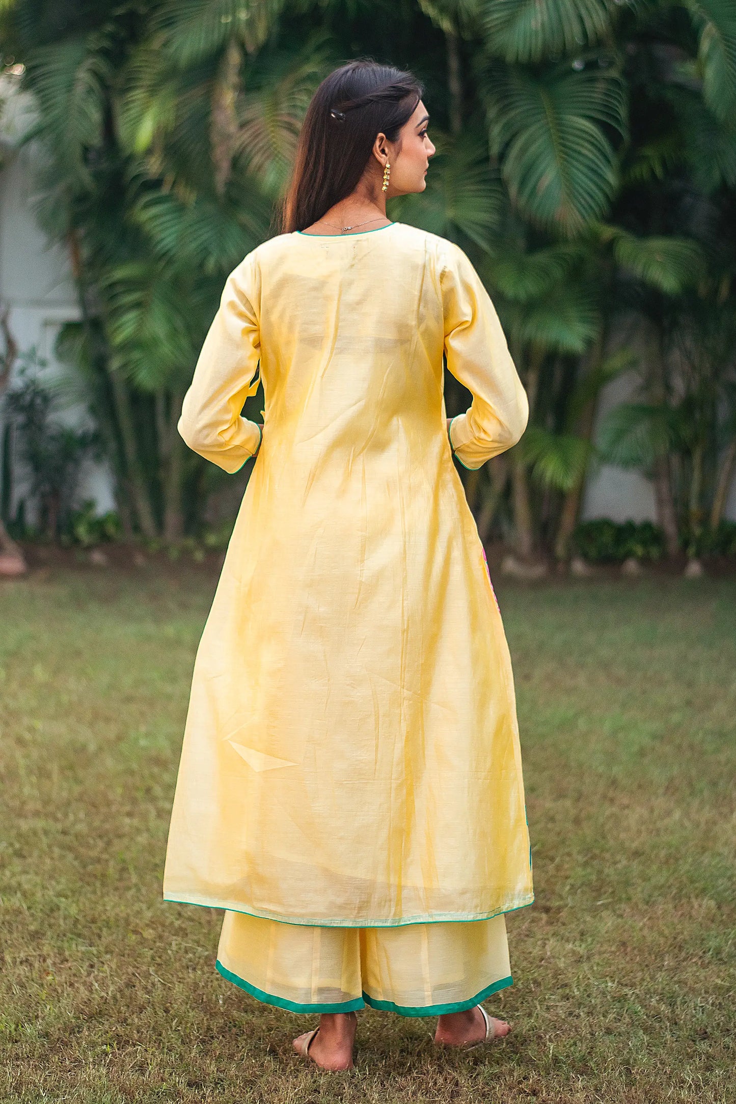 Back view of an Indian model in a yellow angrakha kurta adorned with resham embroidery, paired with matching yellow palazzo.