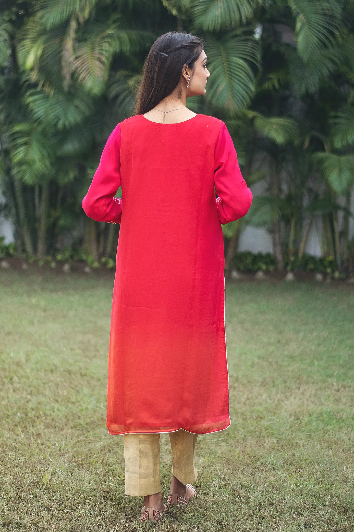 Back view of an Indian model wearing a red organza kurta with gold cutwork, paired with gold brocade trousers.