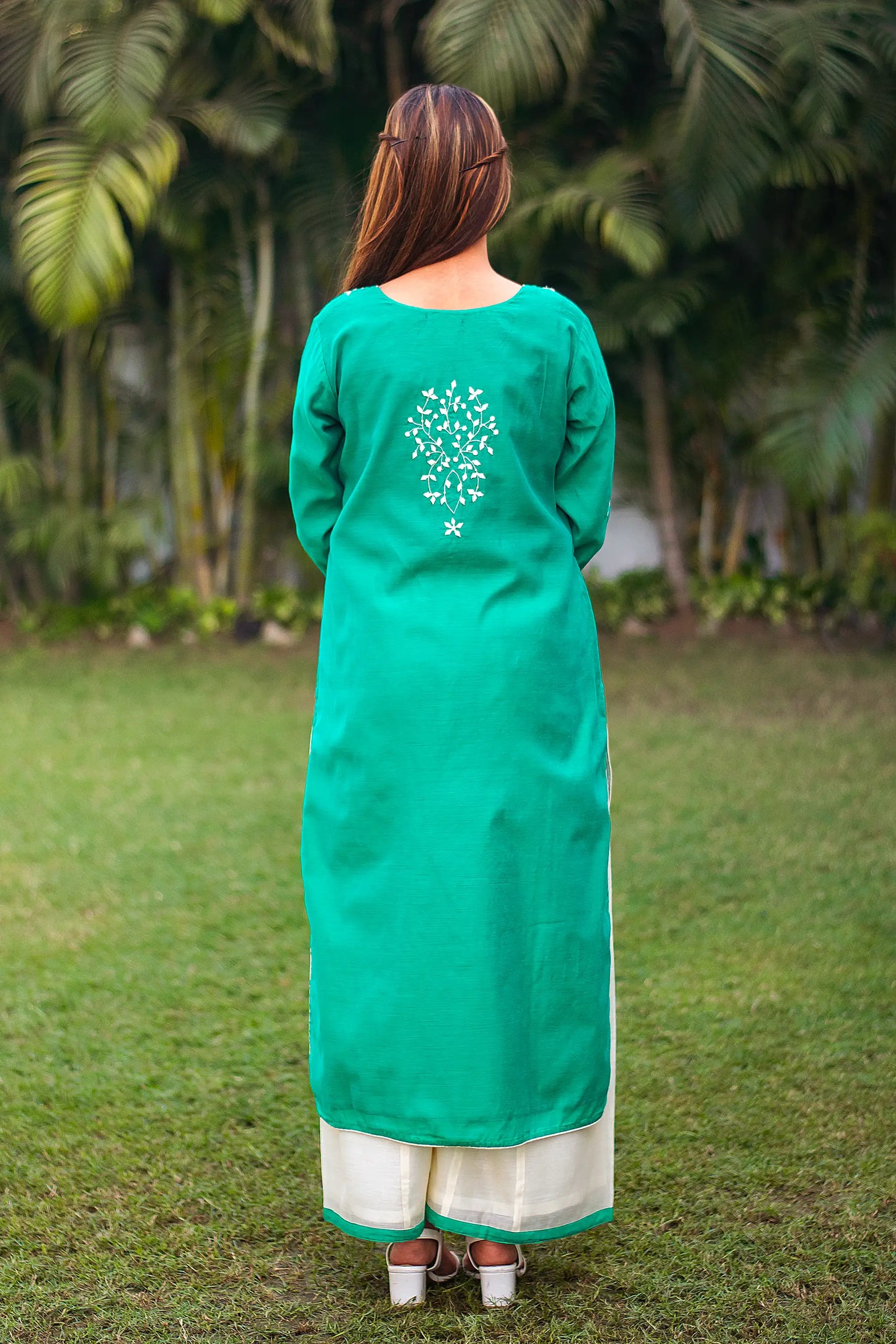 Indian girl poses where the back side of the green Chanderi kurta with applique work and white palazzo is visible.