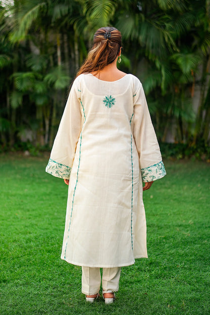 Back view of an Indian model wearing an off-white kurta with a green embroidered flower at the back, paired with matching trousers.