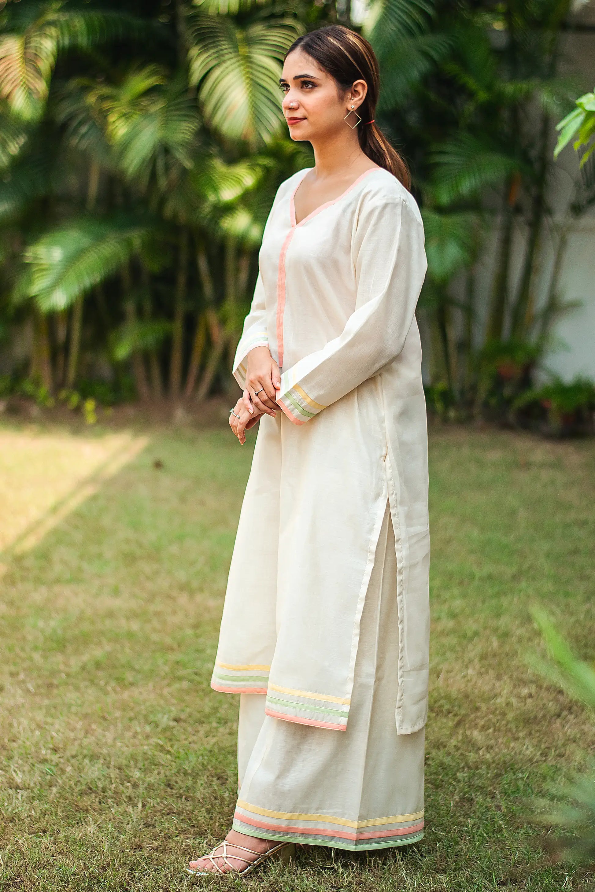 2) Indian model in a side pose, wearing an off-white kurta with peach, green, and yellow piping, paired with off-white palazzo.