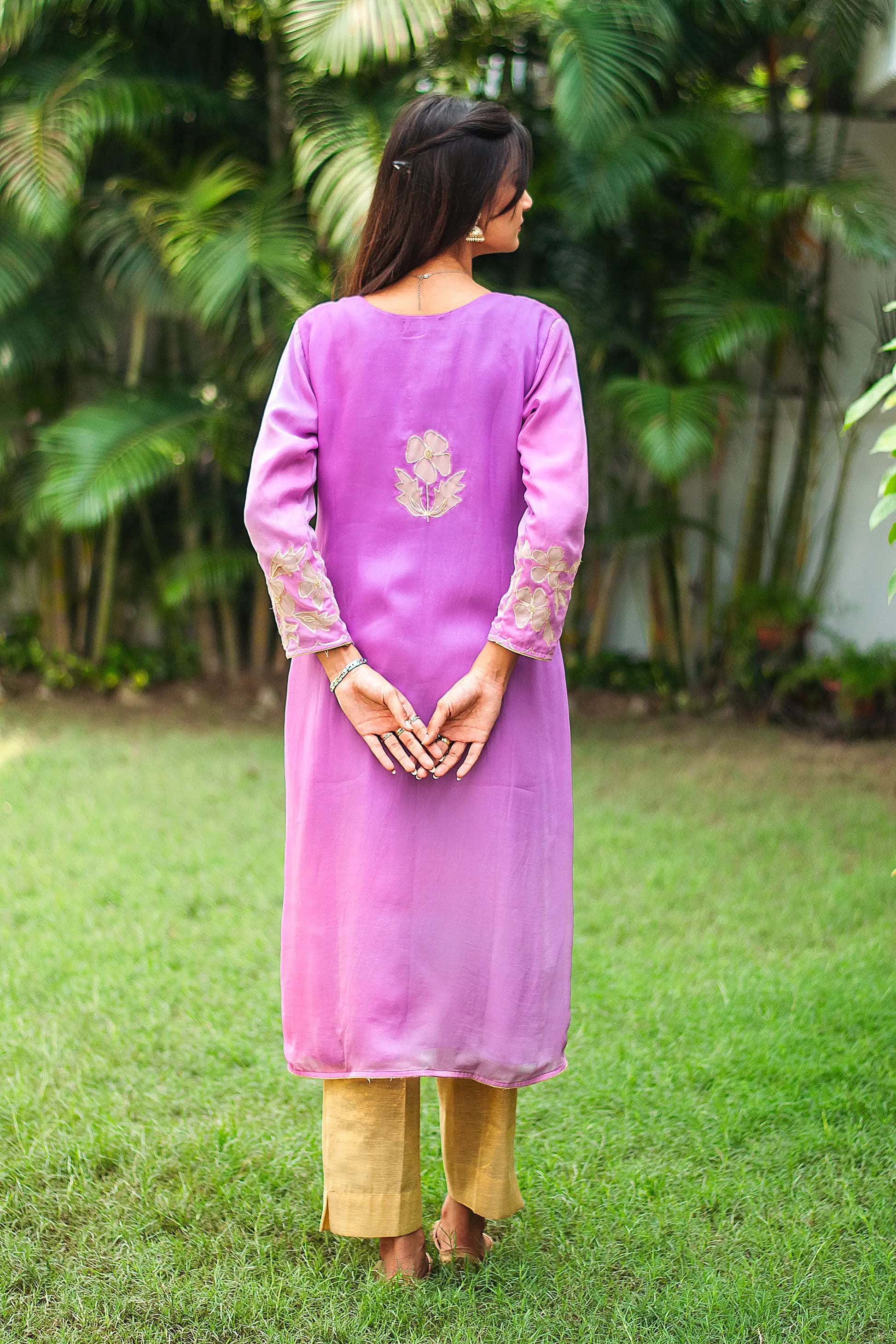 Back view of an Indian model wearing a light purple organza kurta, with a straight silhouette and golden floral cutwork motif at the back.