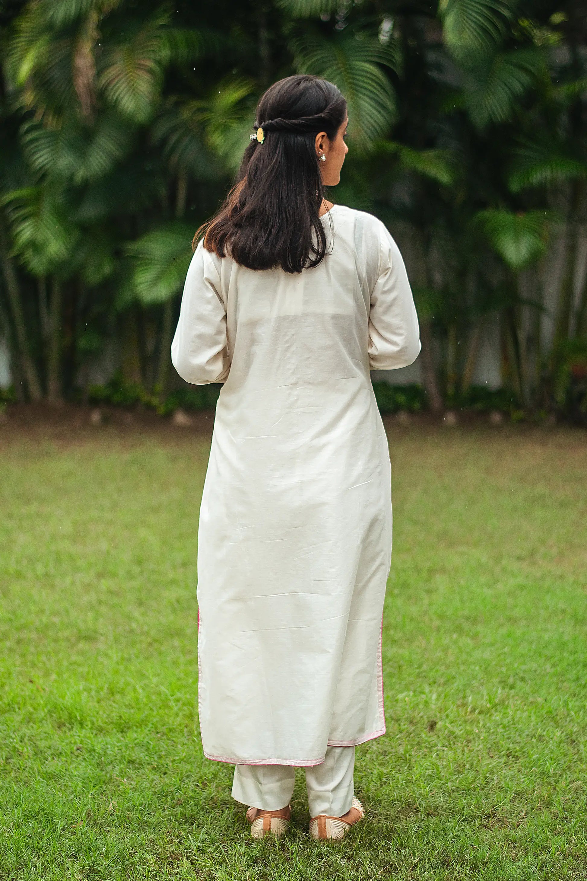 Back view of an Indian model in an off-white chanderi kurta featuring pink floral cutwork and sequins.