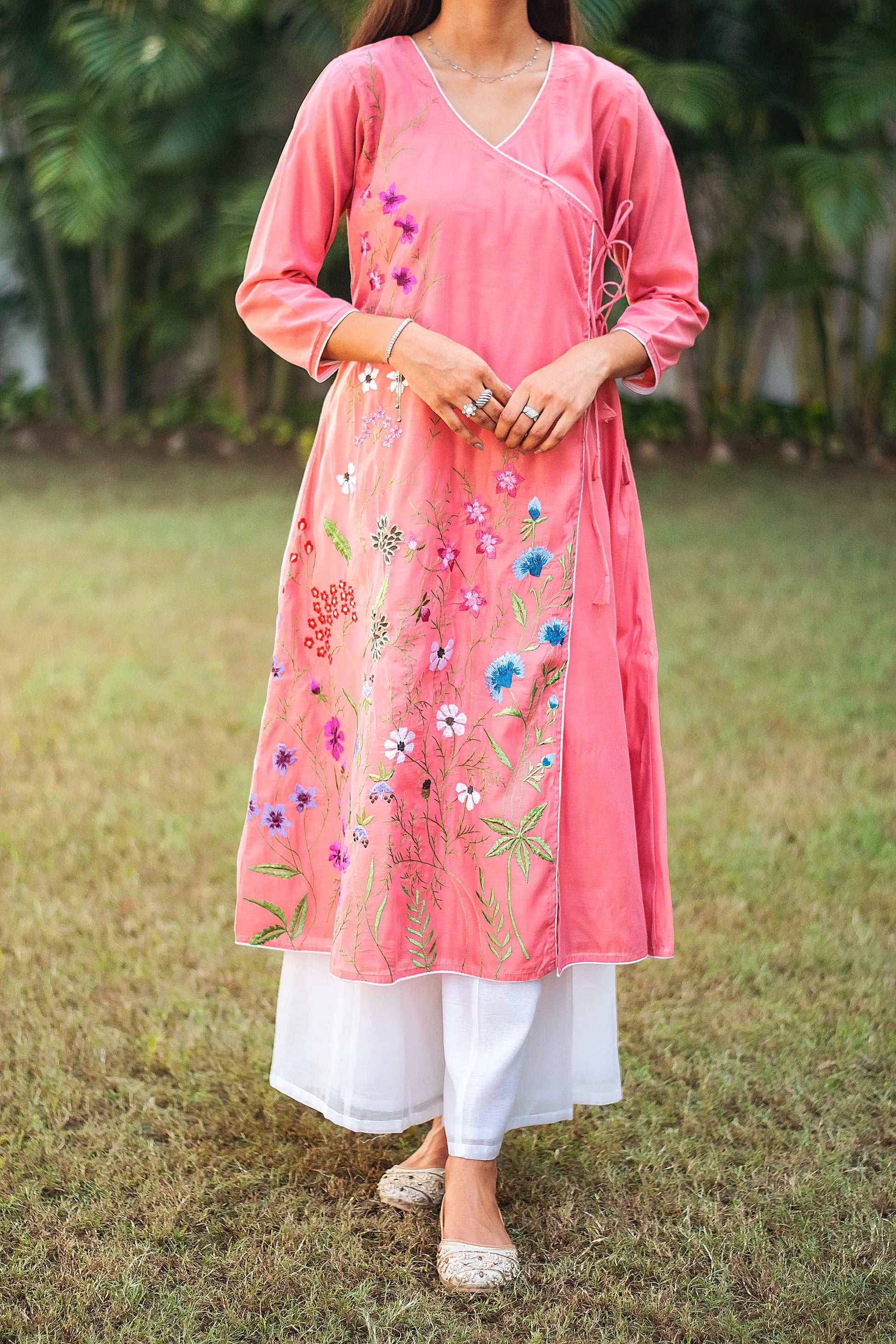 Close up view of a model wearing the pink chanderi kurta set, featuring a pink chanderi angrakha with floral embroidery and white palazzo.