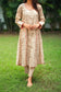 An indian woman wearing a printed staple tussar gold A line kurta and trousers. The A line kurta has double kali in red colour.The woman is facing the camera but her face is not visible, the entire focus is on the ensemble.