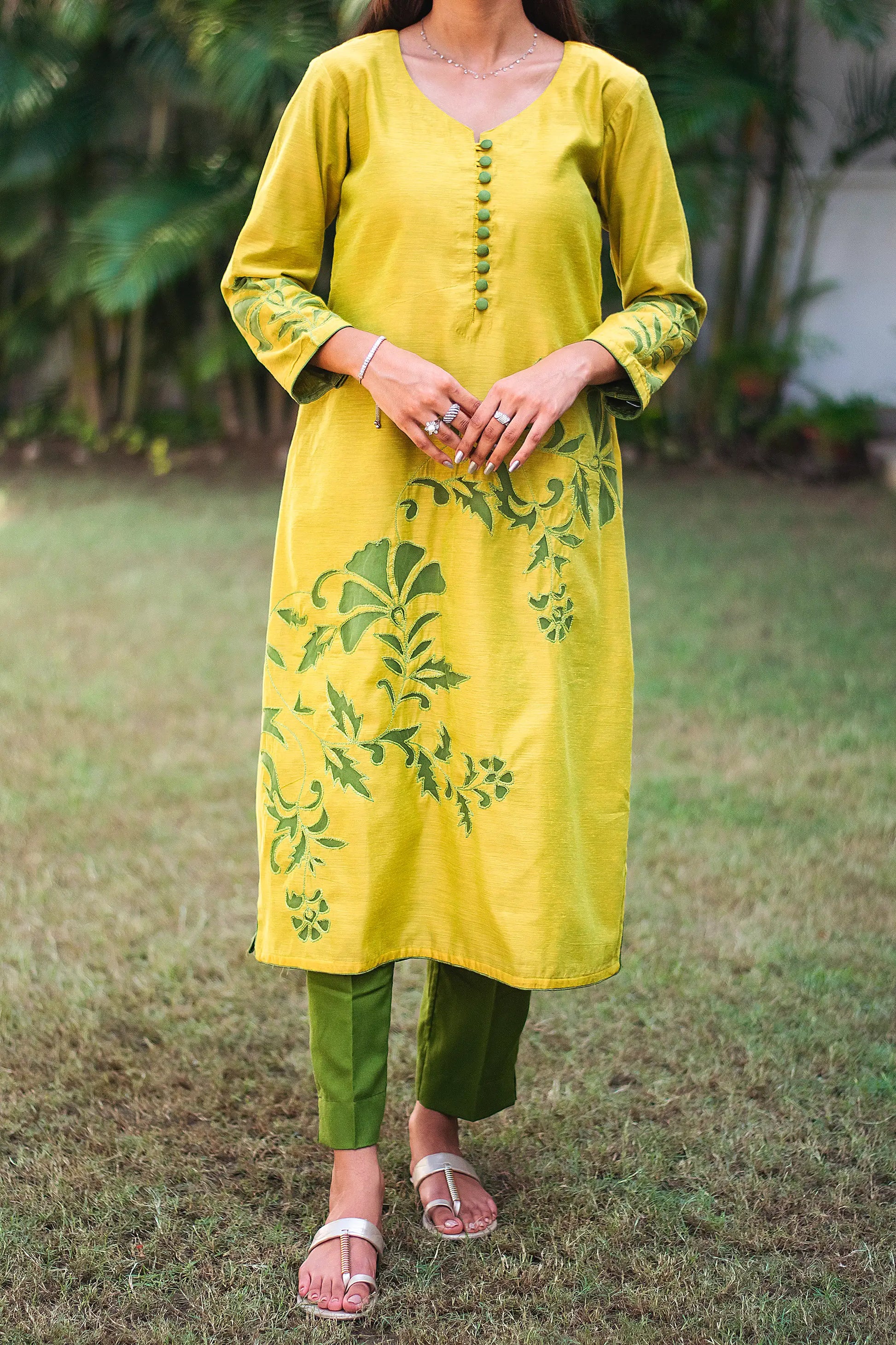 Close up view of a model wearing the cutwork kurta set, featuring a yellowish-green chanderi kurta with green floral cutwork and dark green trousers