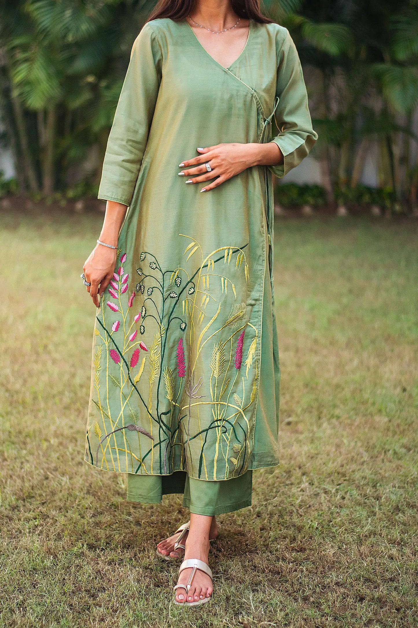 Close up view of a model wearing the green kurta set, featuring a green chanderi angrakha with floral embroidery and green palazzo