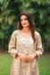 An indian woman wearing a printed staple tussar gold A line kurta and trousers with gold chanderi dupatta. The A line kurta has double kali in red colour. The woman is facing the camera and the attire is visible from neck till the torso