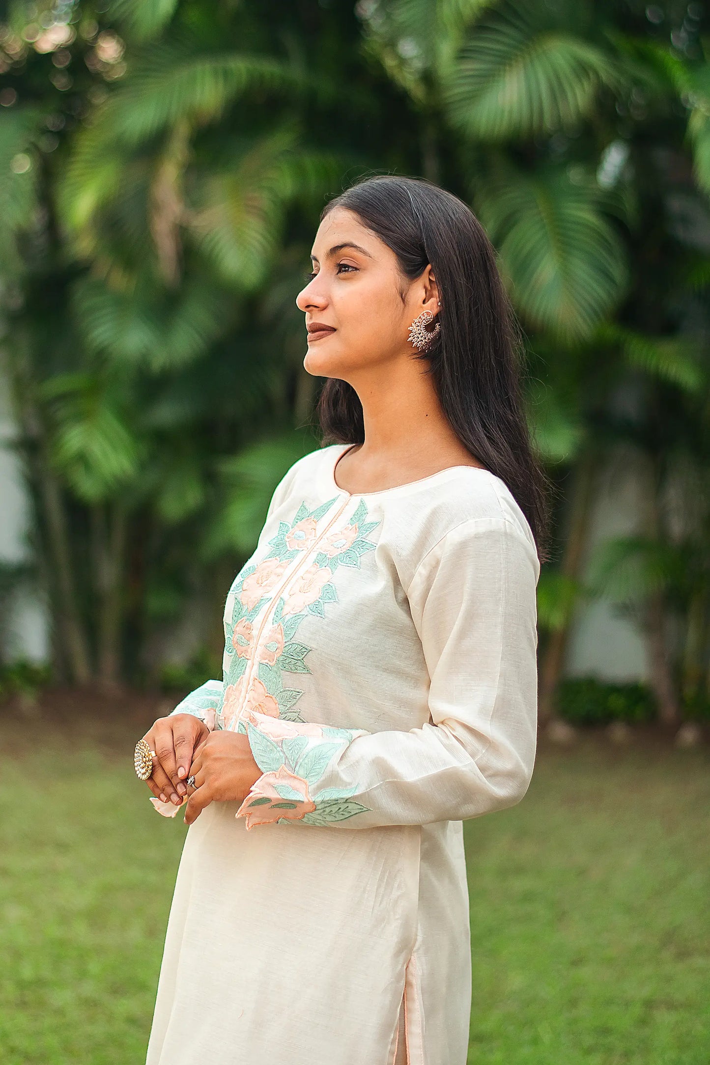 Side view of an Indian model in a cream chanderi kurta with peach floral patchwork on the sleeves and yoke.