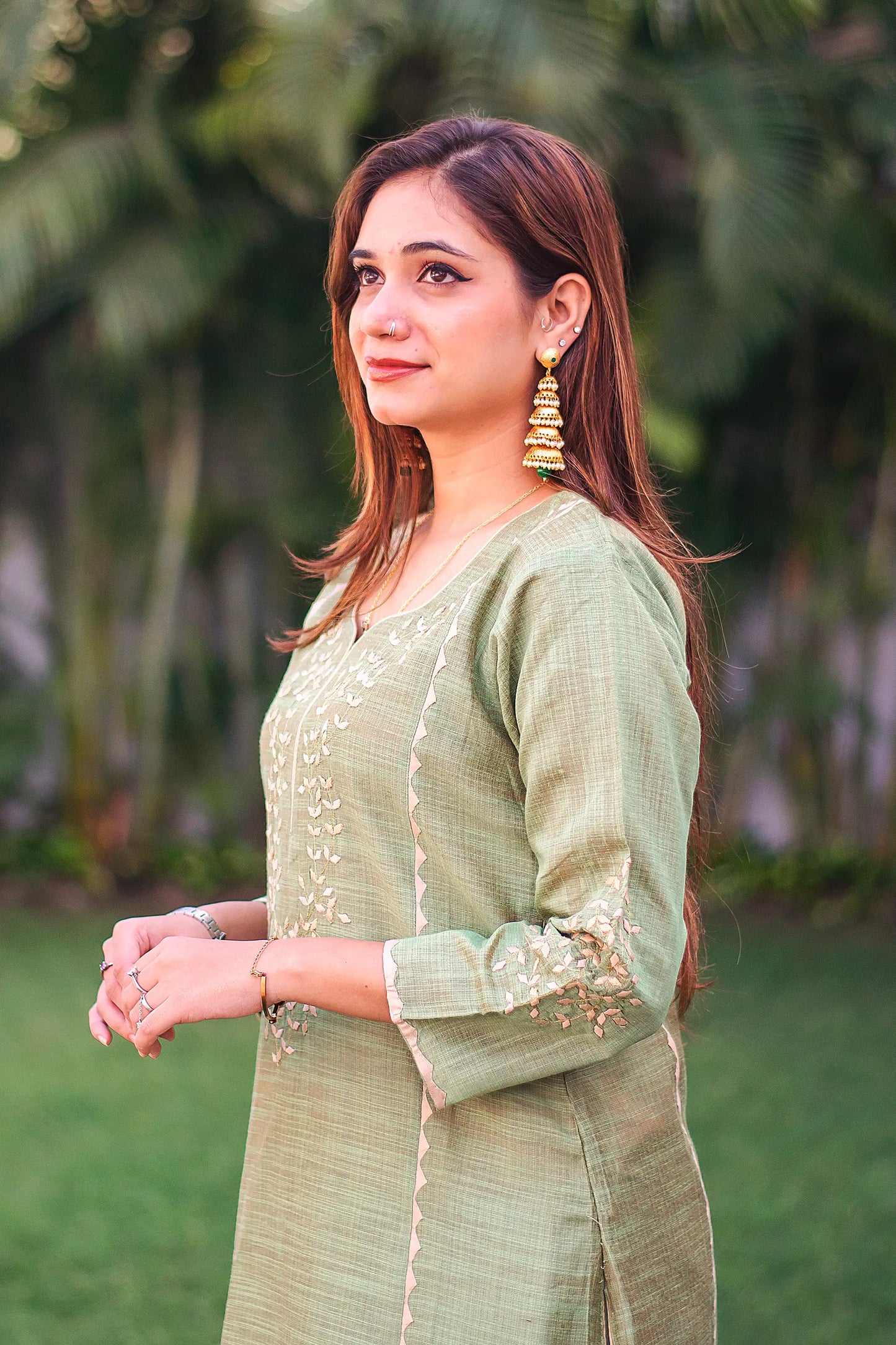 Side view of an Indian model in a green jute silk kalidar kurta with beige applique work.