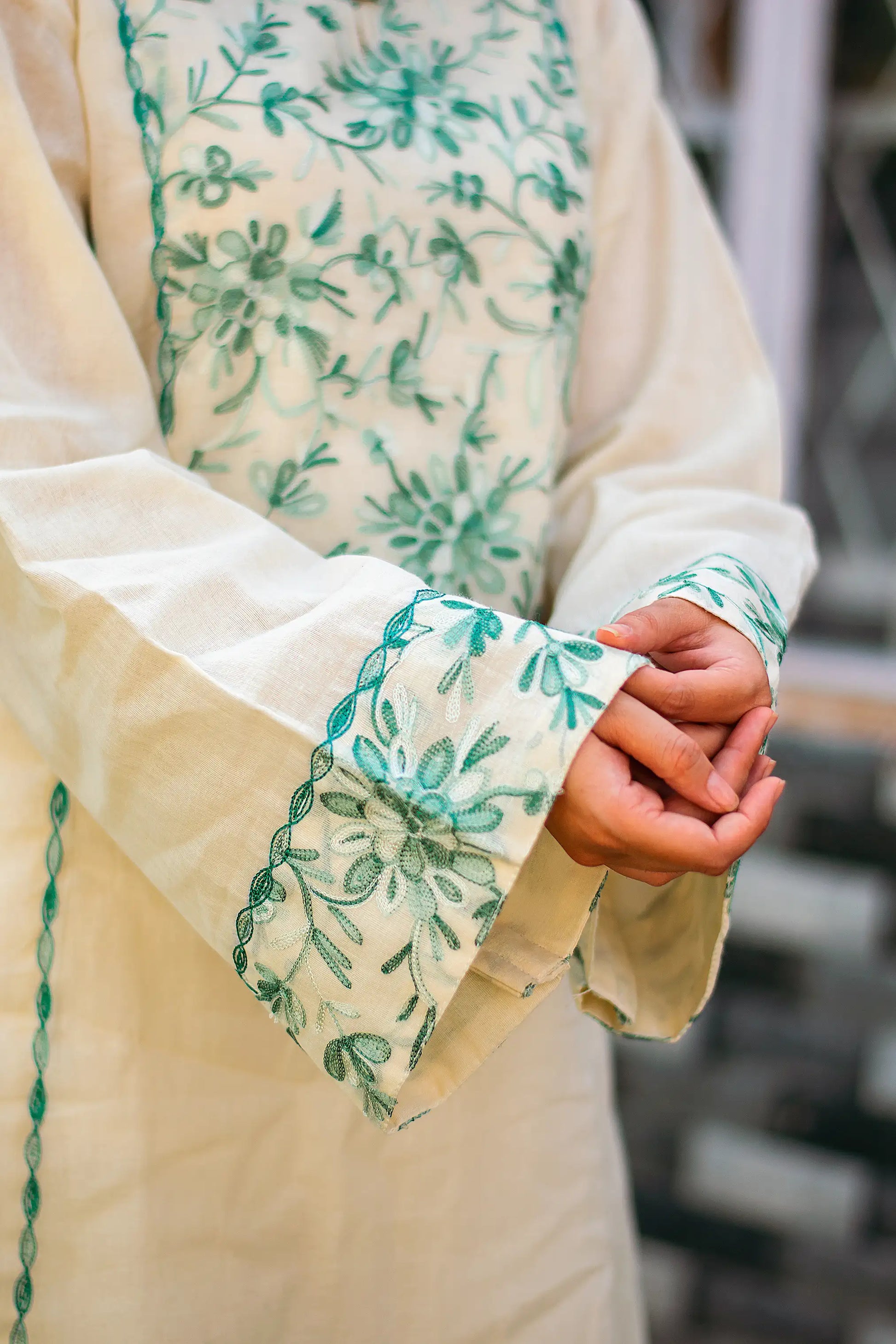 Detailed view of green Kashmiri embroidery on the sleeve cuff of the off-white kurta.