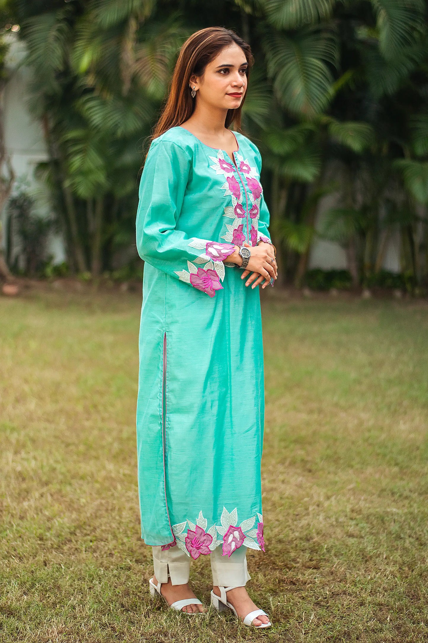 Side view of an Indian model wearing a blue chanderi kurta with purple patchwork flowers, paired with off-white trousers. 