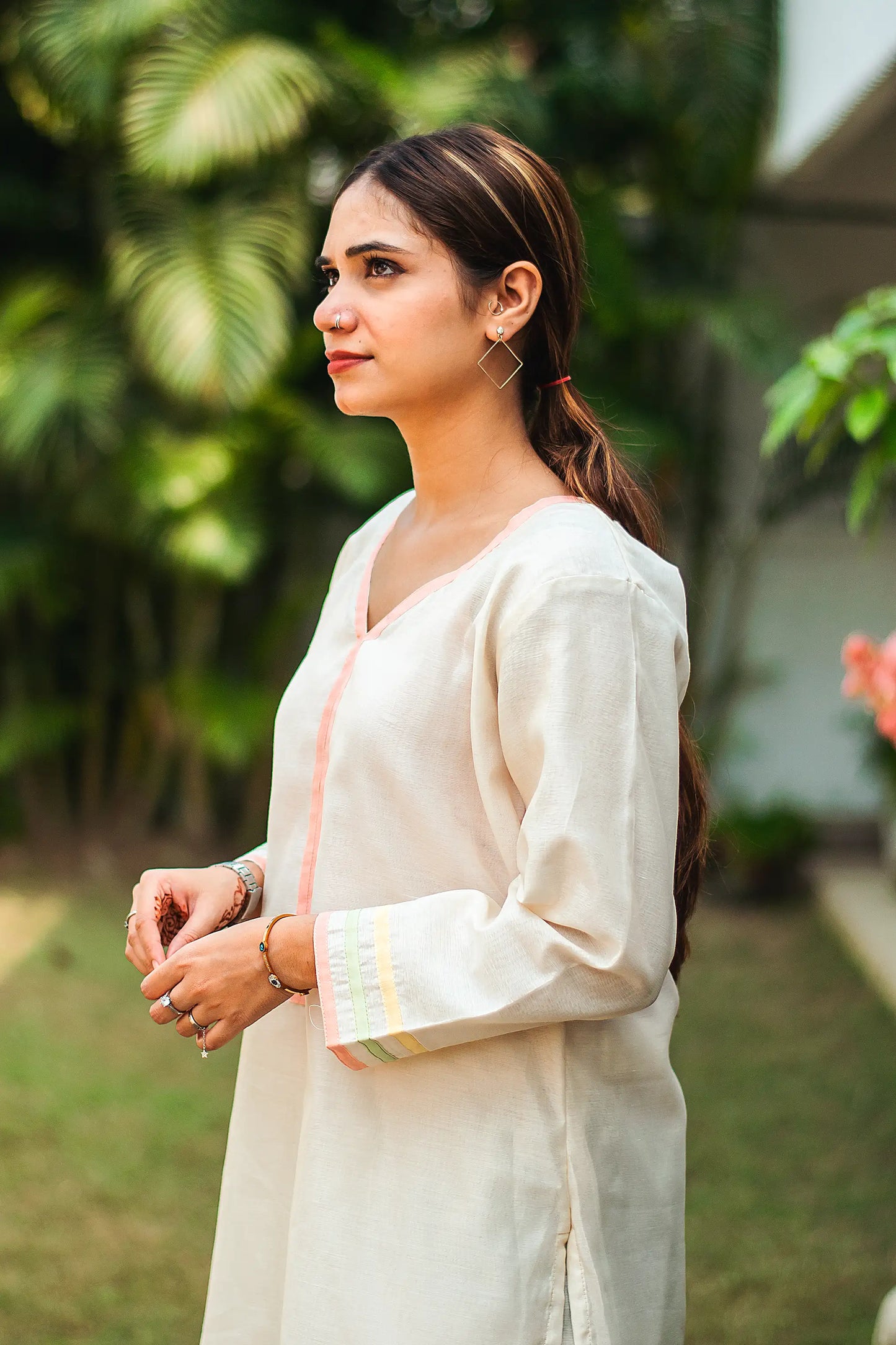 1) Side pose of an Indian model wearing an off-white chanderi kurta with pastel piping along the yoke,  hem and cuffs.