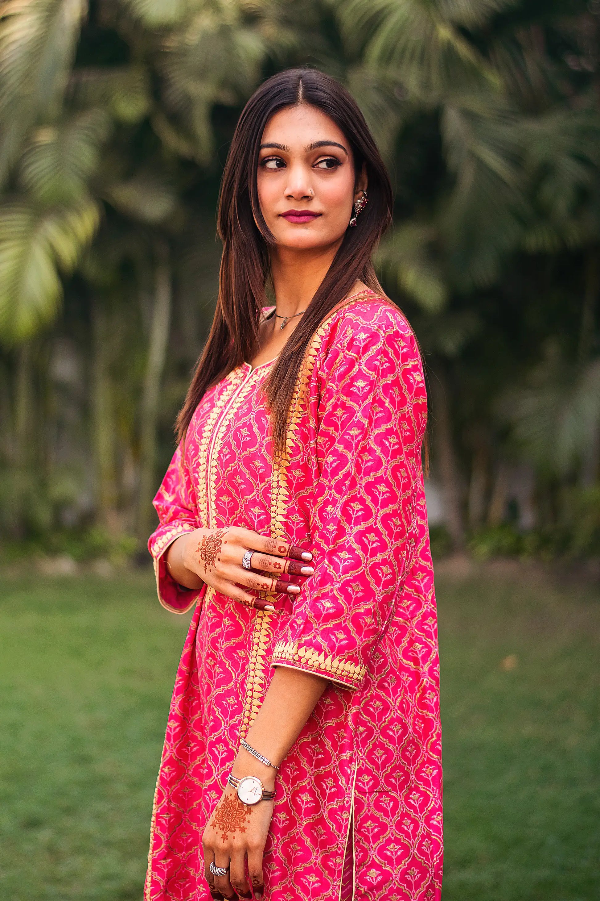 . Indian model poses sideways in a magenta kalidar kurta with beige applique.