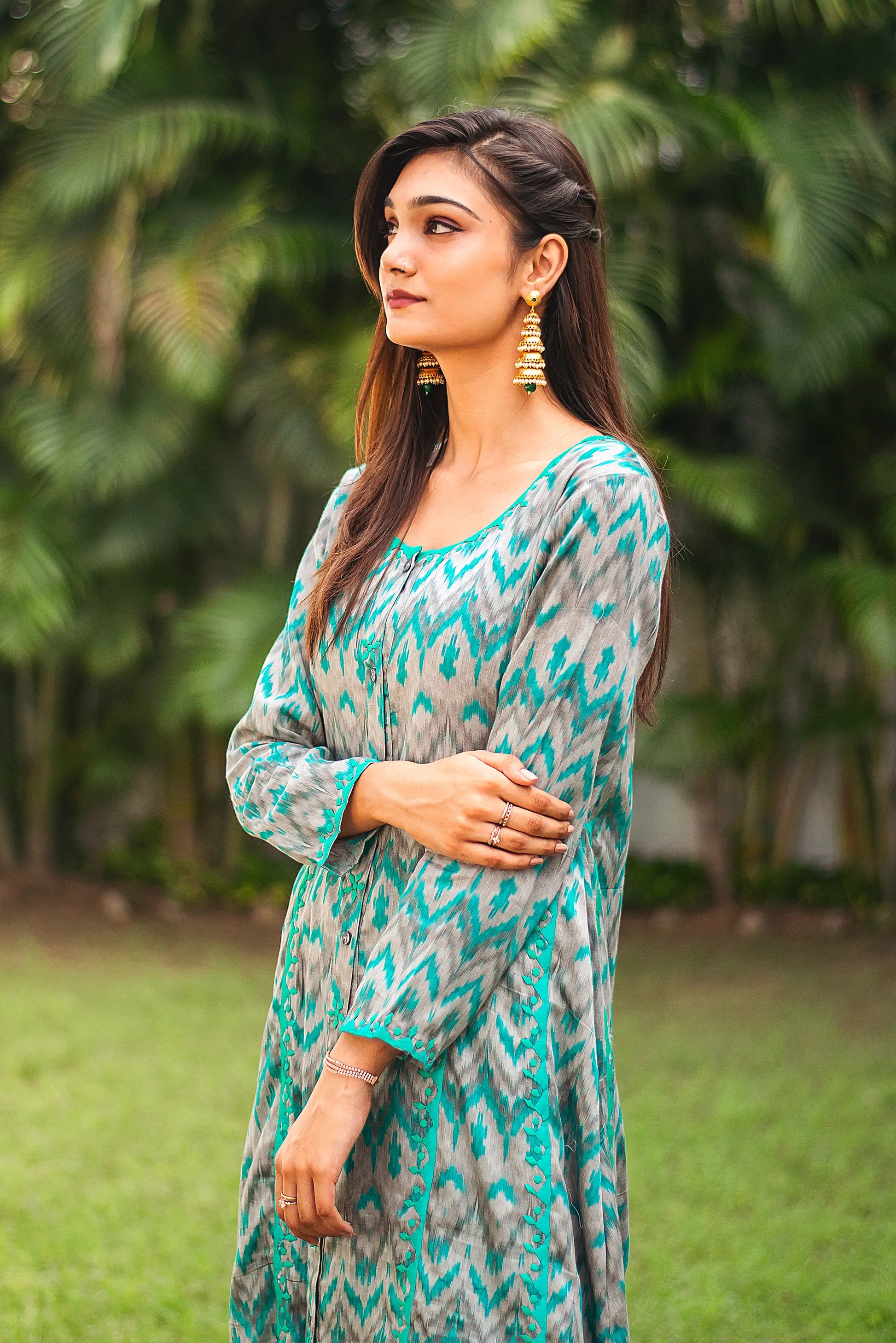 Side view of an Indian model in a grey and green ikat print kurta with green applique motifs along the hem and cuffs.