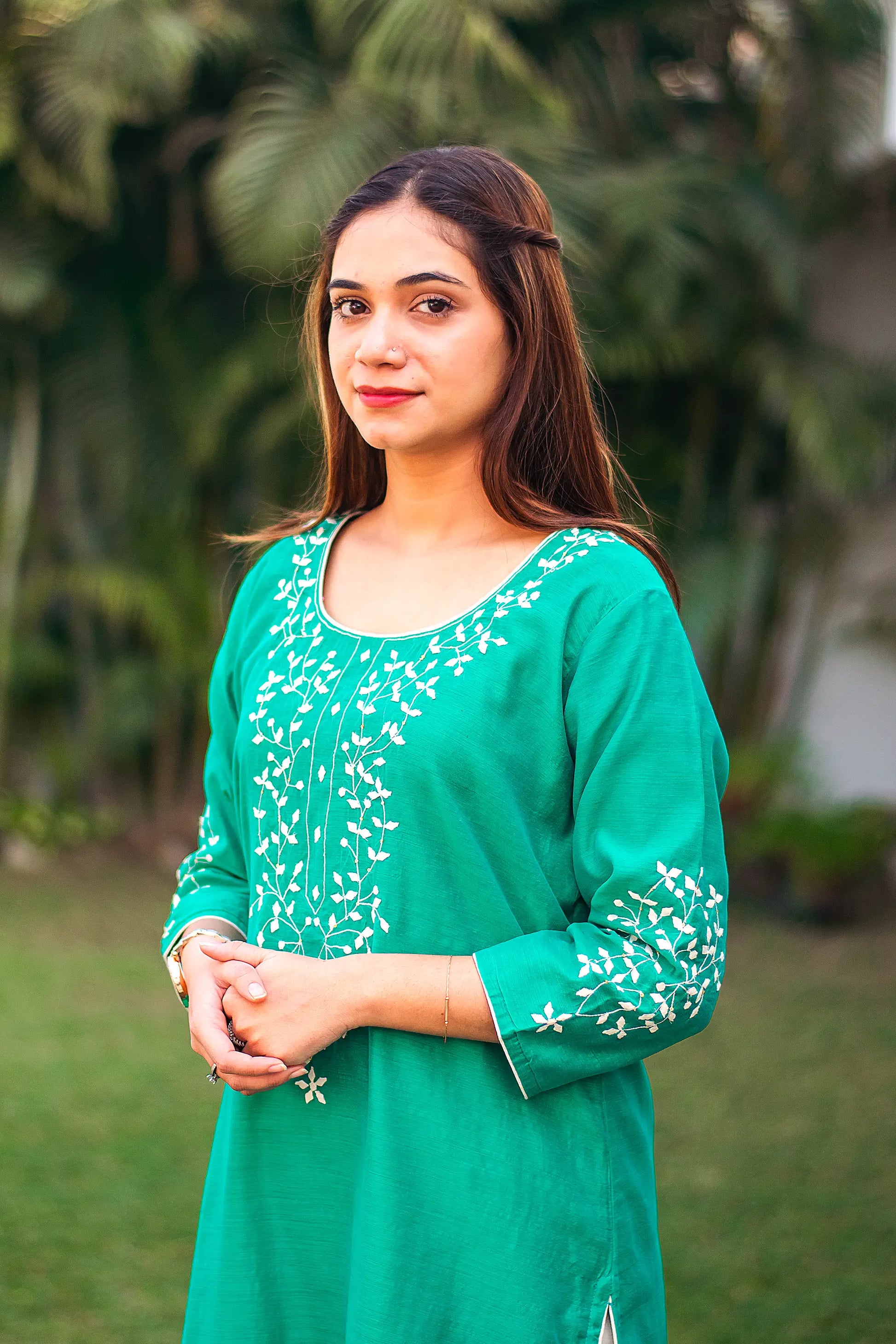 An Indian girl in a left side pose wearing a green Chanderi kurti with applique work, upper half is visible.