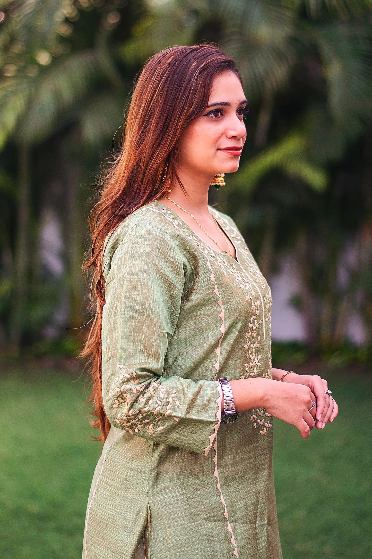 Indian model in a side pose, wearing a green jute silk kalidar kurta with intricate beige applique work.