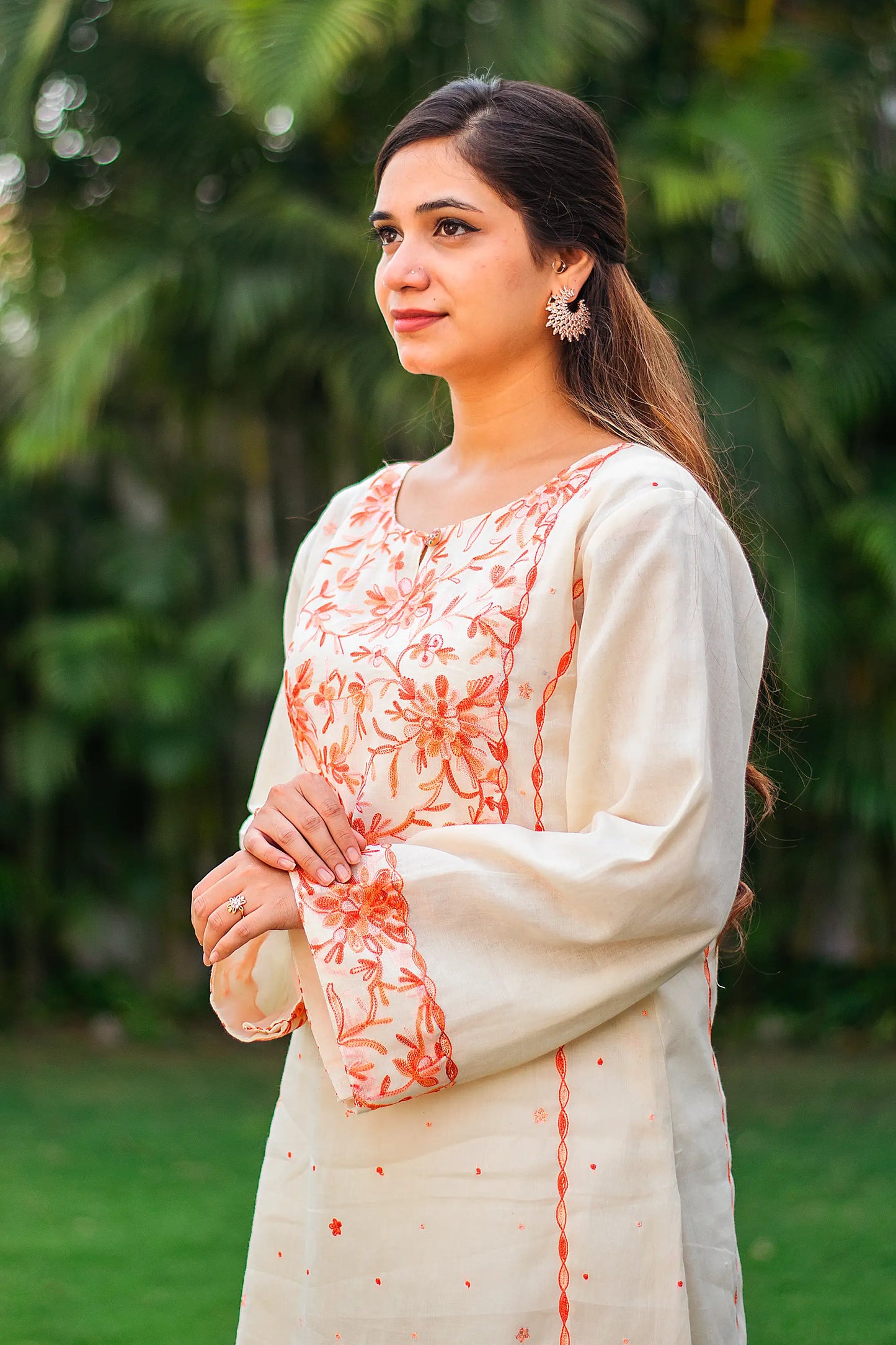 Side view of an Indian model in an off-white kalidar kurta with peach Kashmiri embroidery. 