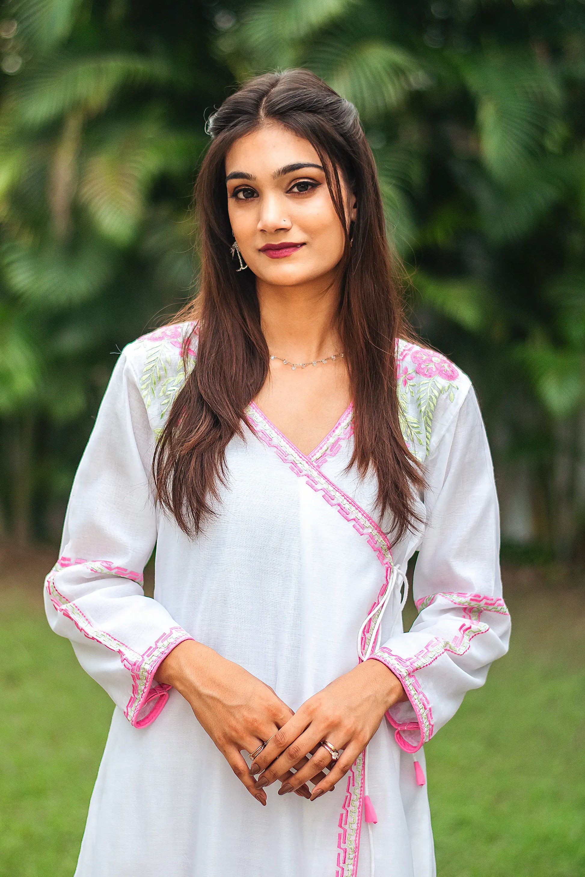 Close-up of the model focusing on the pink floral and green leaf embroidery on the yoke of the white chanderi angrakha.