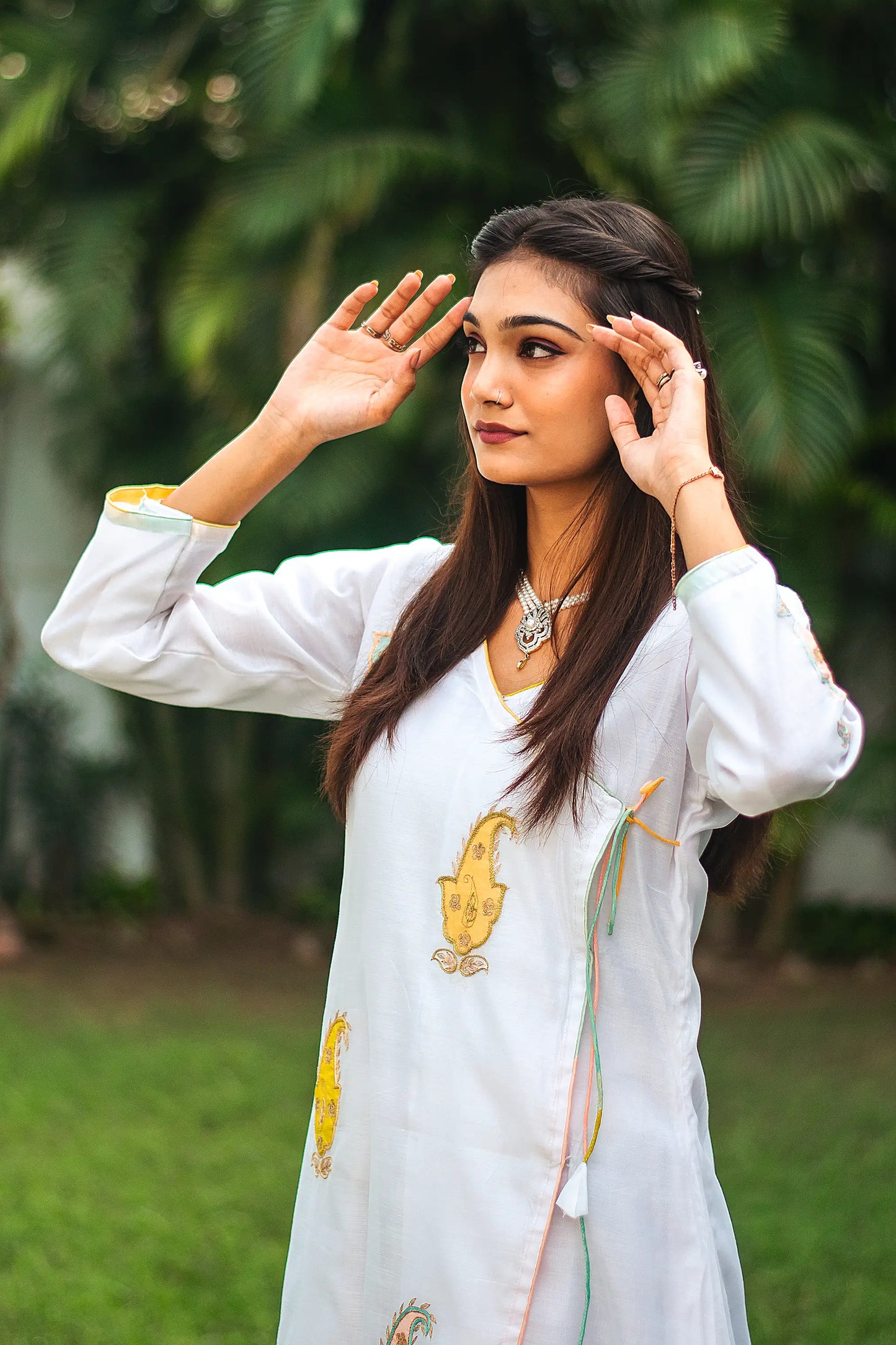 Side pose of an Indian model in a white chanderi angarkha kurta having kairi (paisley) patchwork.