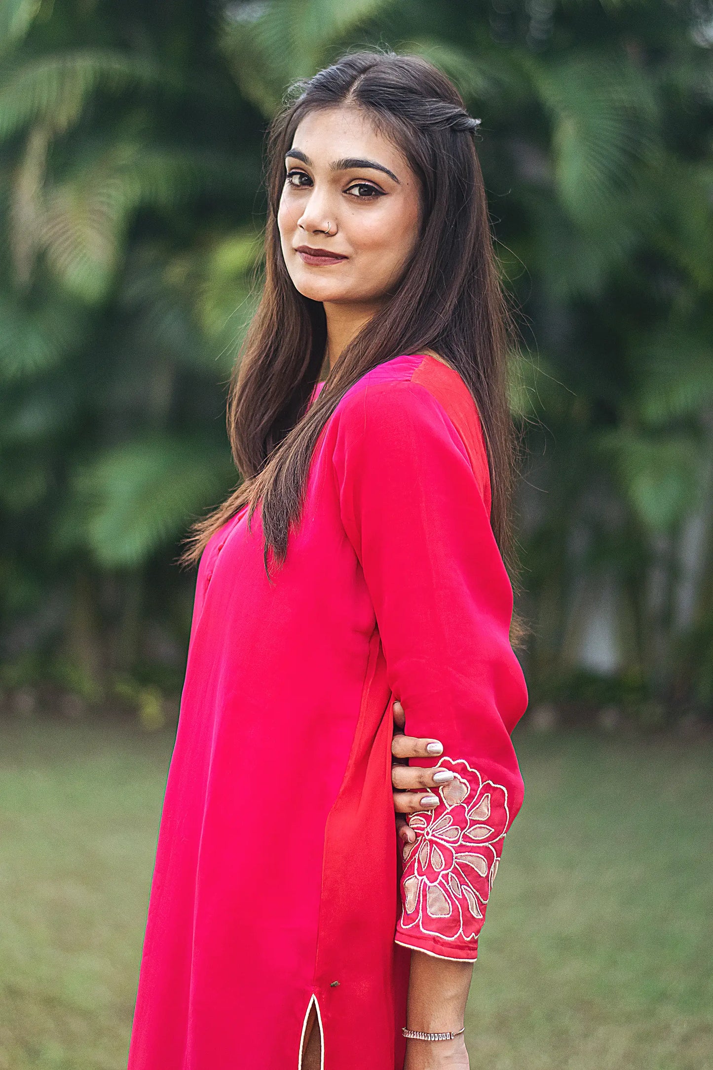 Side pose of an Indian model wearing a red organza kurta with opulent gold cutwork along the cuff is visible.