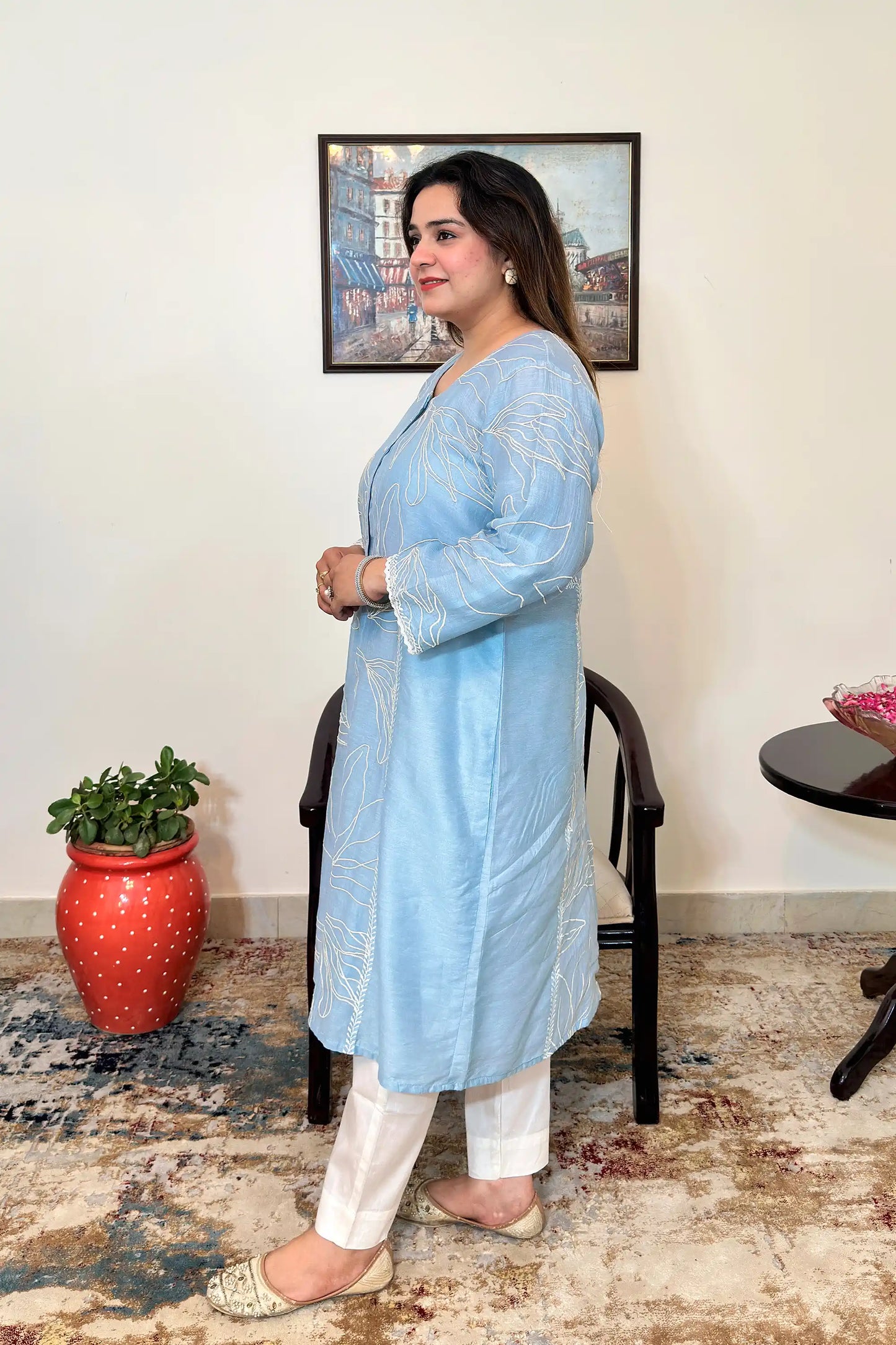 Side view of the blue chanderi A-line kurta with white floral resham embroidery, worn with off-white trousers, dupatta off.