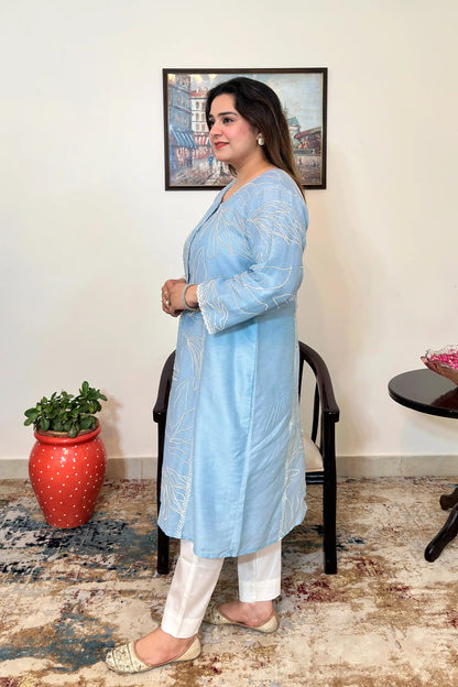 Side view of the blue chanderi A-line kurta with white floral resham embroidery, worn with off-white trousers, dupatta off.