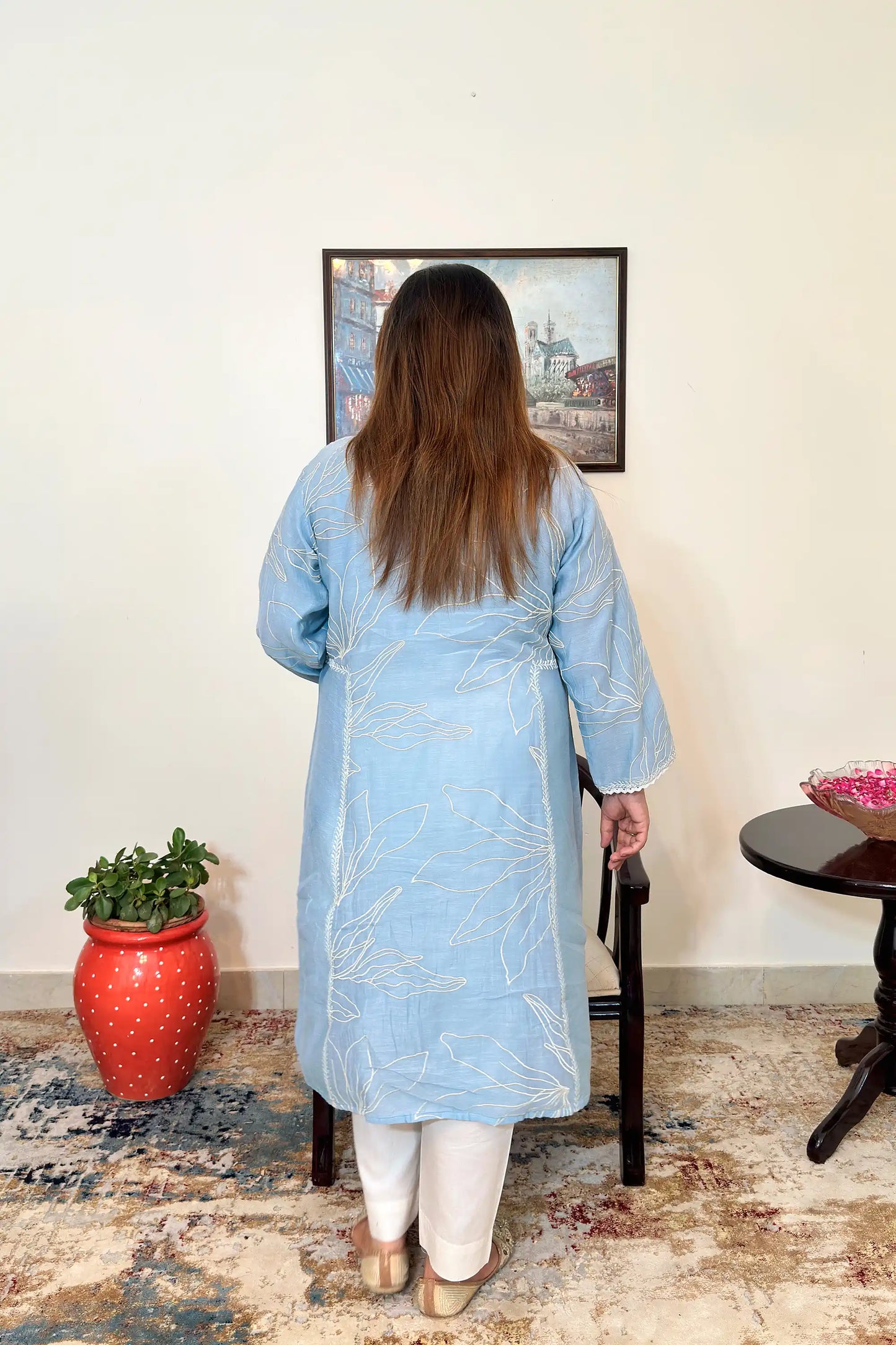 Back view of the blue chanderi A-line kurta with white floral resham embroidery, worn with off-white trousers.