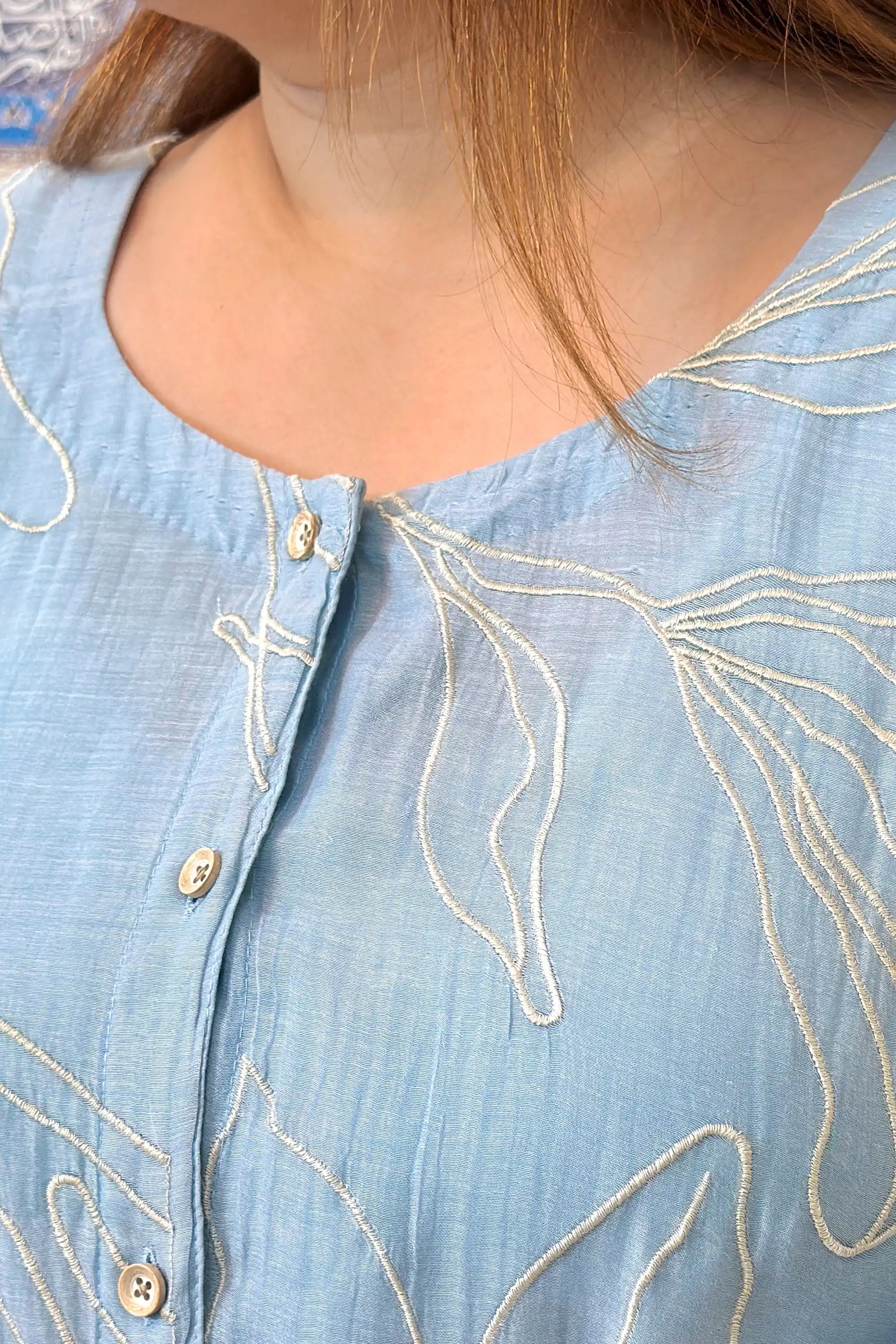 Close-up of the button placket on the blue chanderi kurta, showing white floral resham embroidery detail.