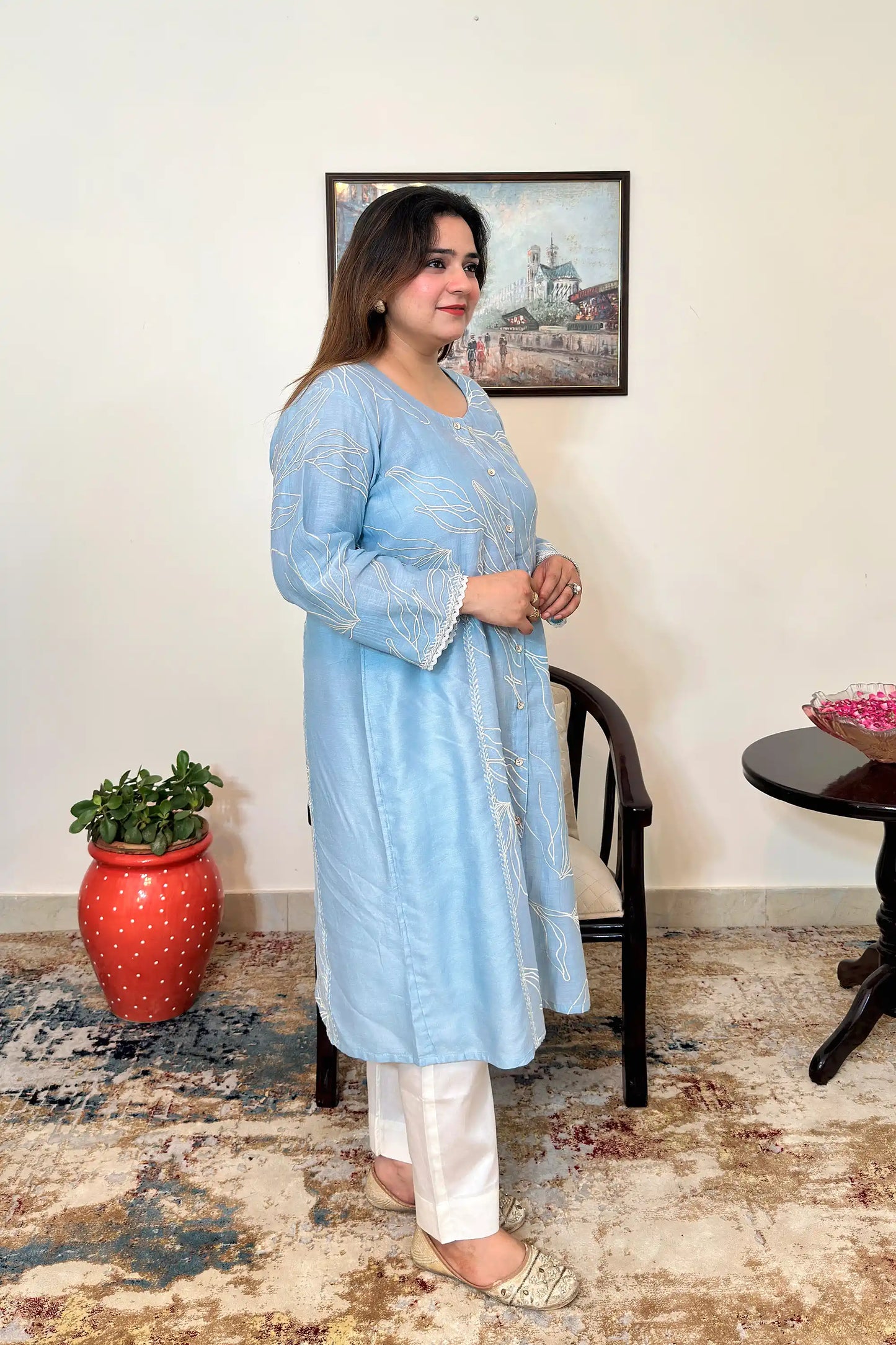 Side view of the blue chanderi A-line kurta with white floral resham embroidery, worn with off-white trousers, dupatta off.
